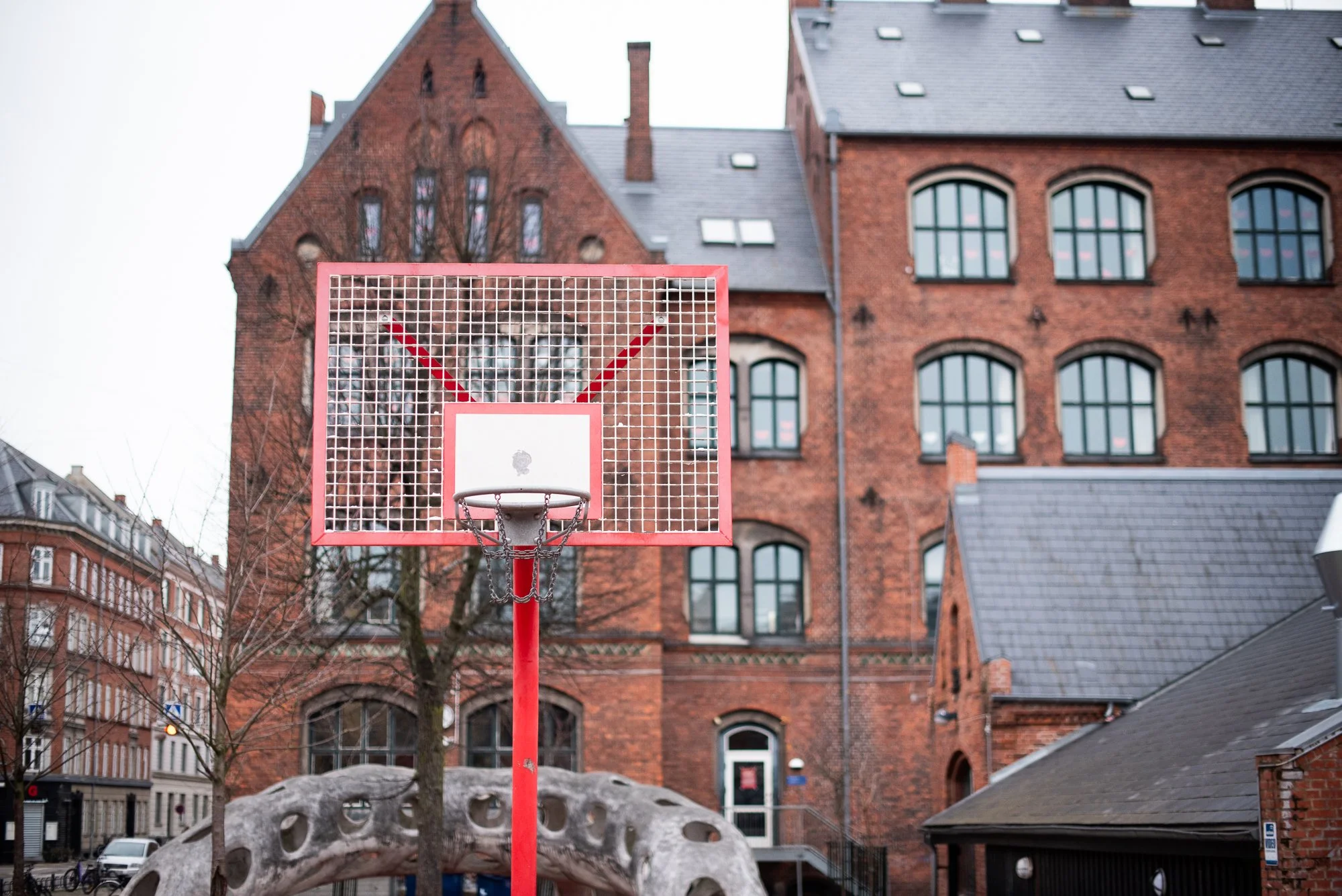 Outdoor basketball hoop with a red backboard set in front of a historic brick building in Europe.
