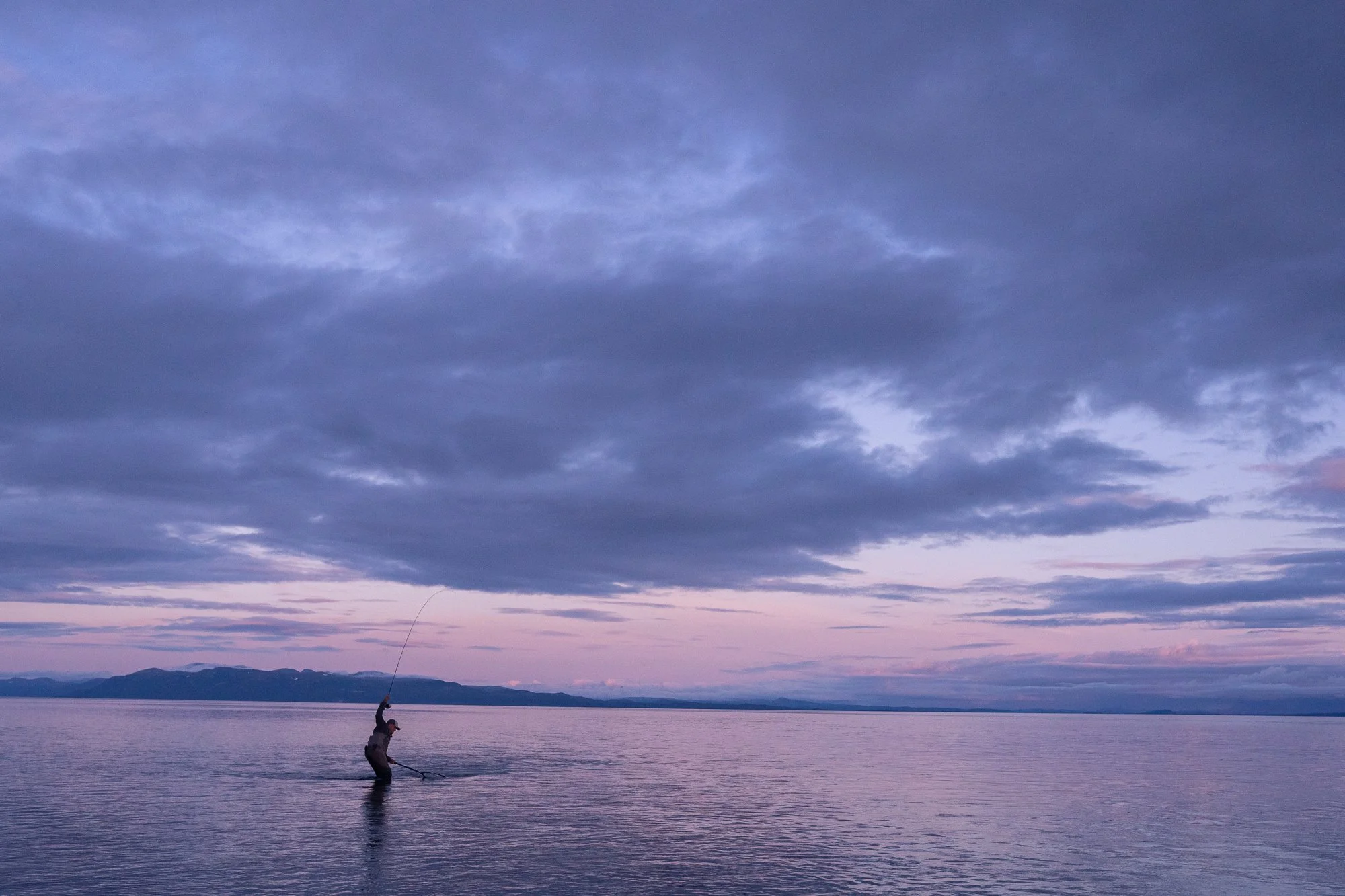 Fly fisherman standing in the water at dusk in Alaska