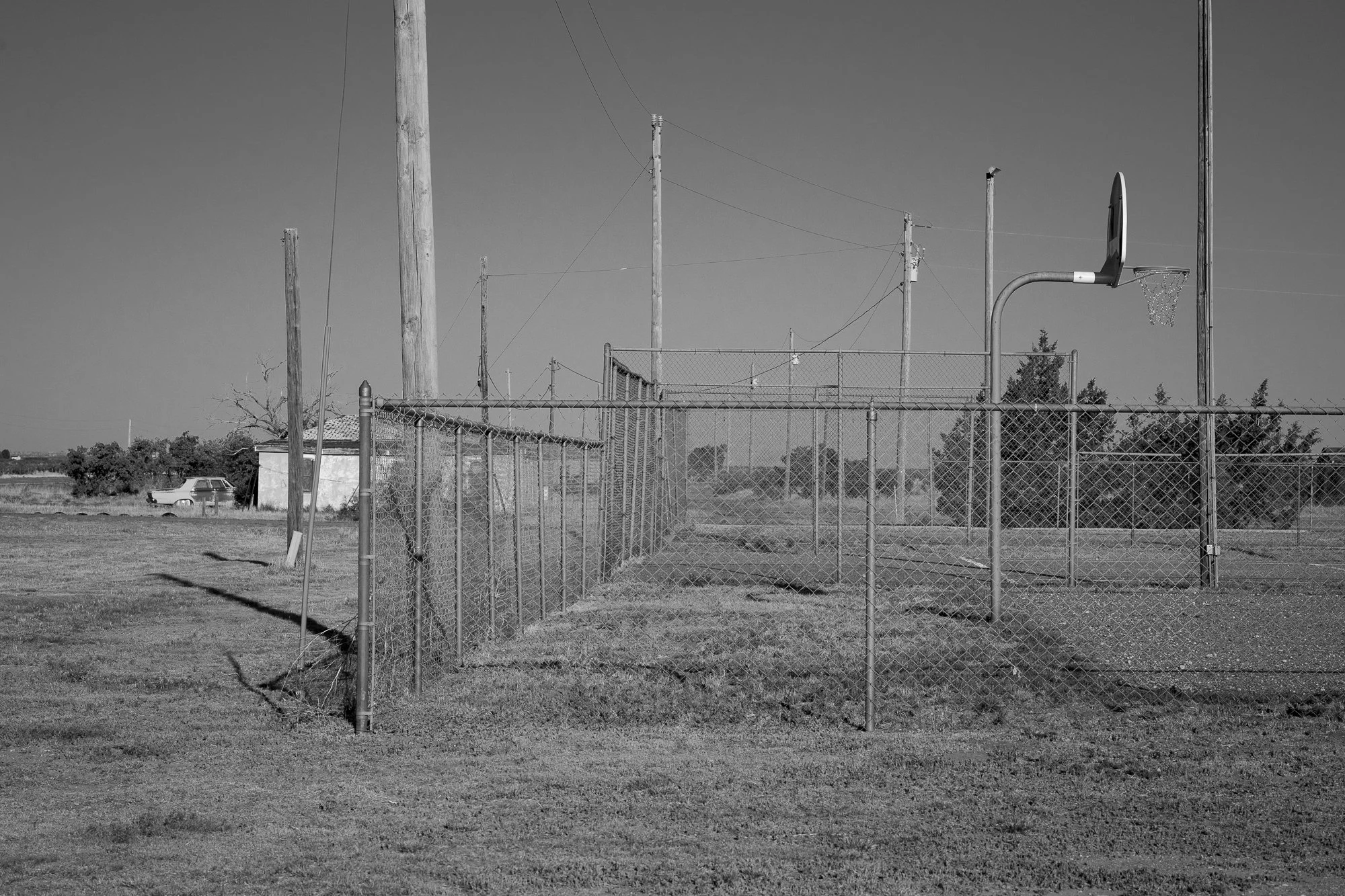 Black and white photograph of a rural basketball hoop behind a chain link fence on the Llano Estacado