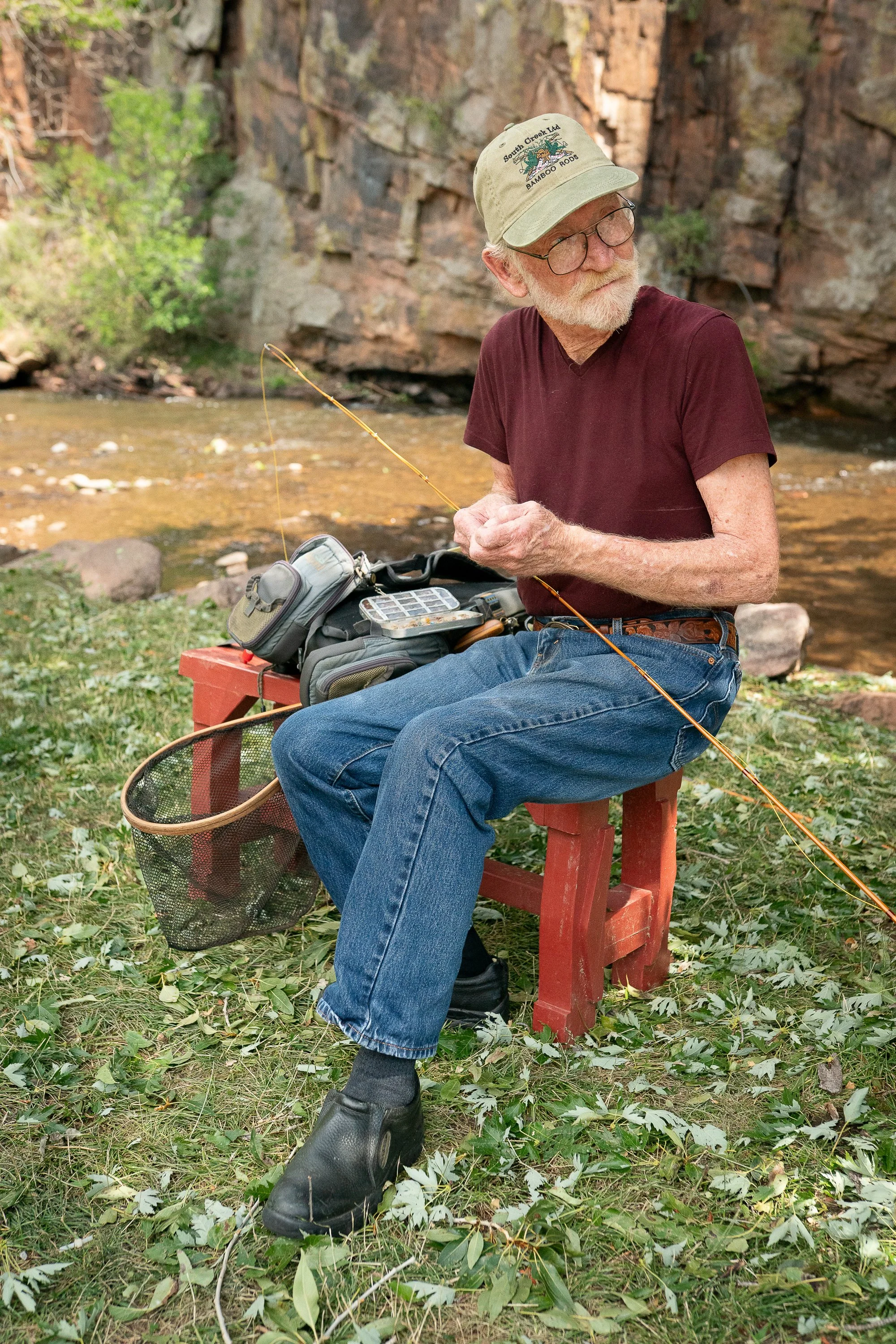 Mike Clark sitting beside a Colorado creek with a bamboo fly rod and fishing gear.