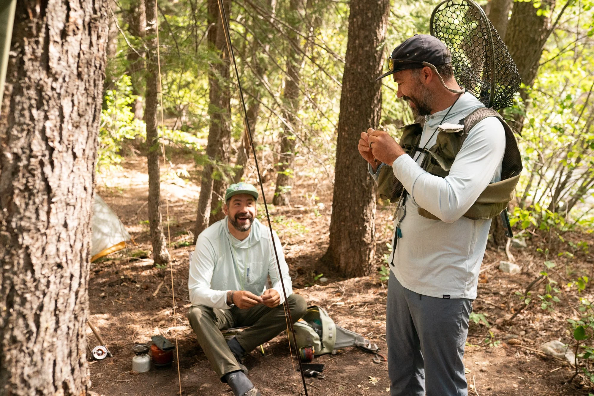 Two fly anglers pause in the trees with rods, packs, and landing nets