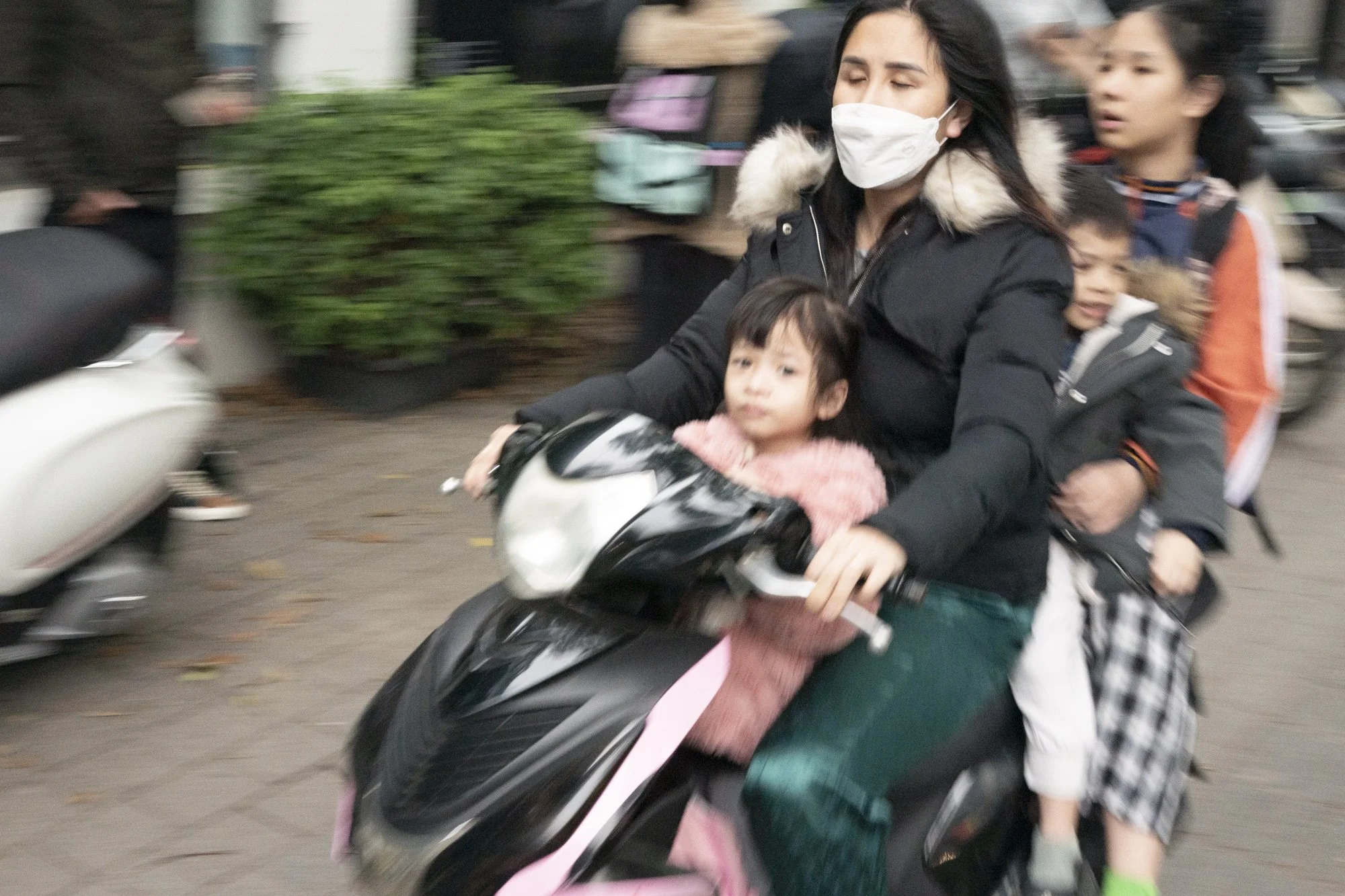 A family of four riding a scooter through the streets of Hanoi Vietnam