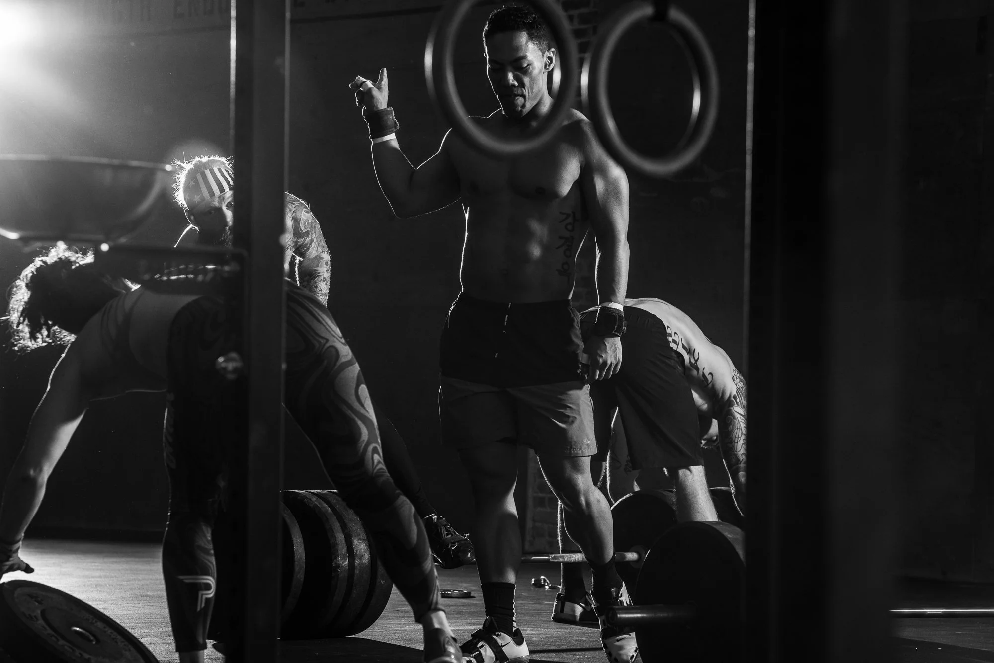 CrossFit athletes working around loaded barbells during a workout inside a gritty gym.