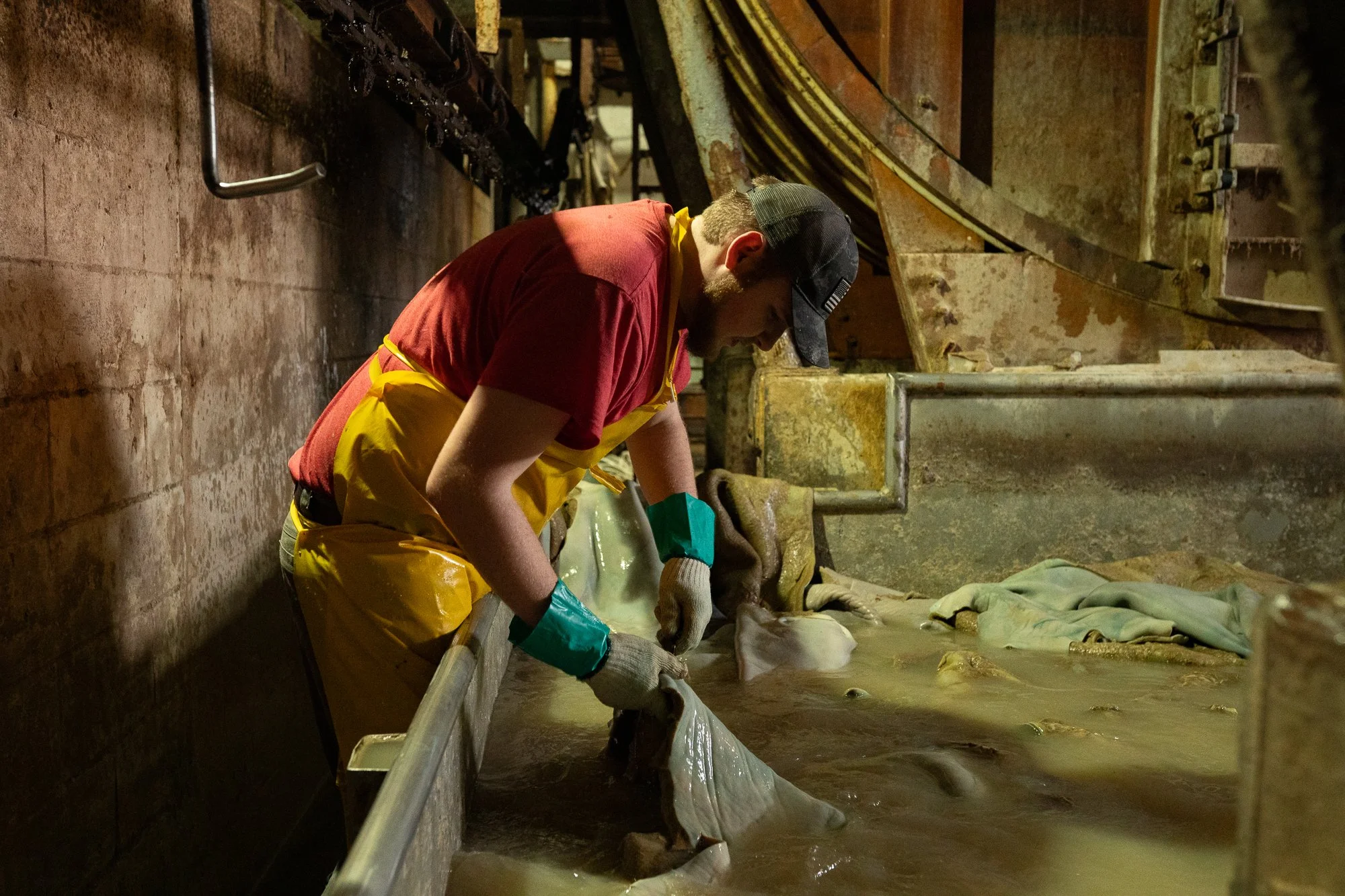A Wickett & Craig worker handles a large wet leather hide beside a metal processing machine inside the Pennsylvania tannery.