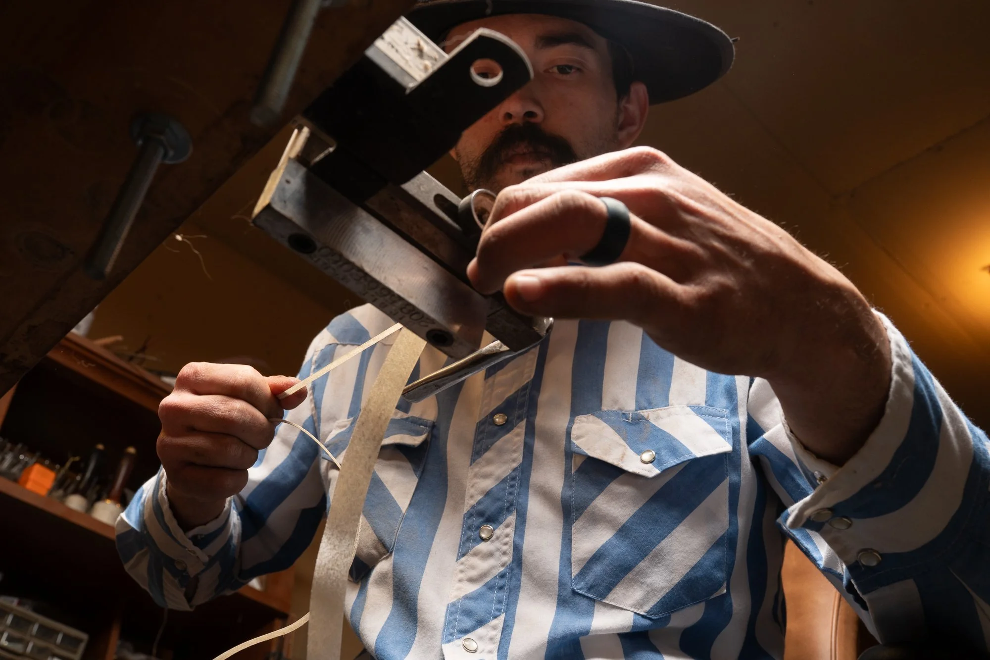 A rawhide strand being guided through a beveling tool by Dakota May during the preparation process