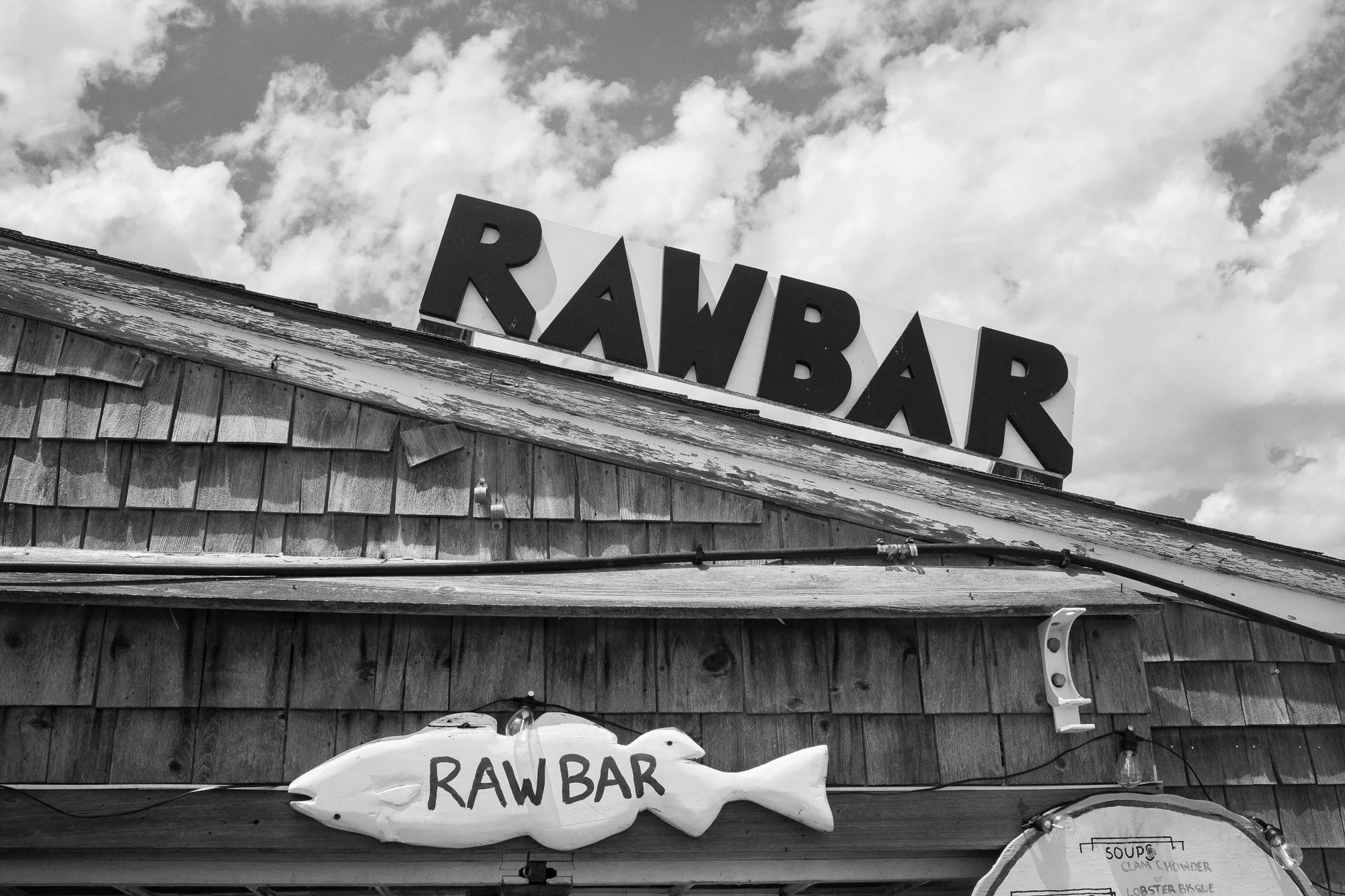 Black and white photo of a Cape Cod seafood shack with raw bar sign and weathered wood exterior