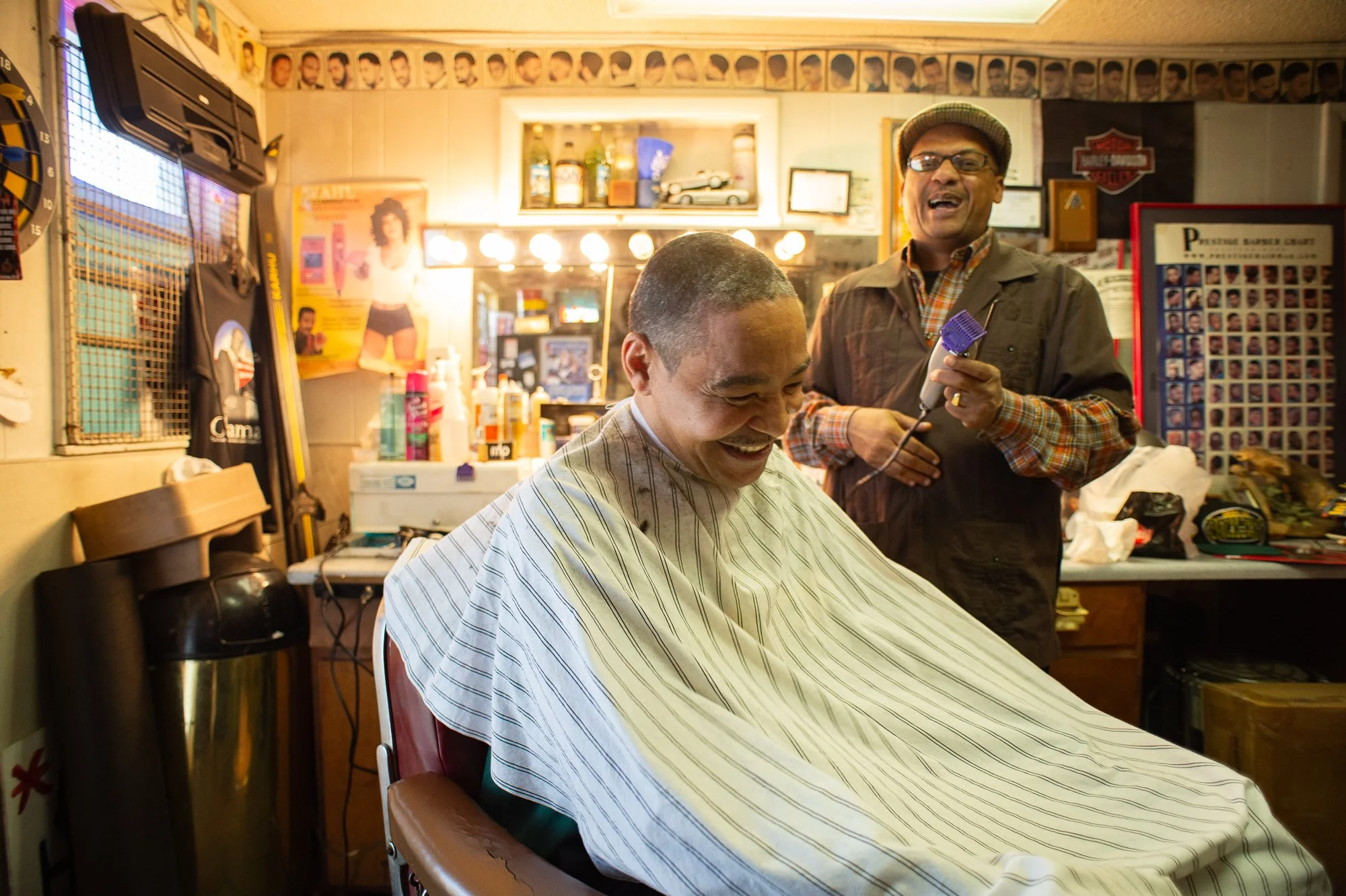 Barber smiling while cutting a client’s hair inside a traditional Black barbershop