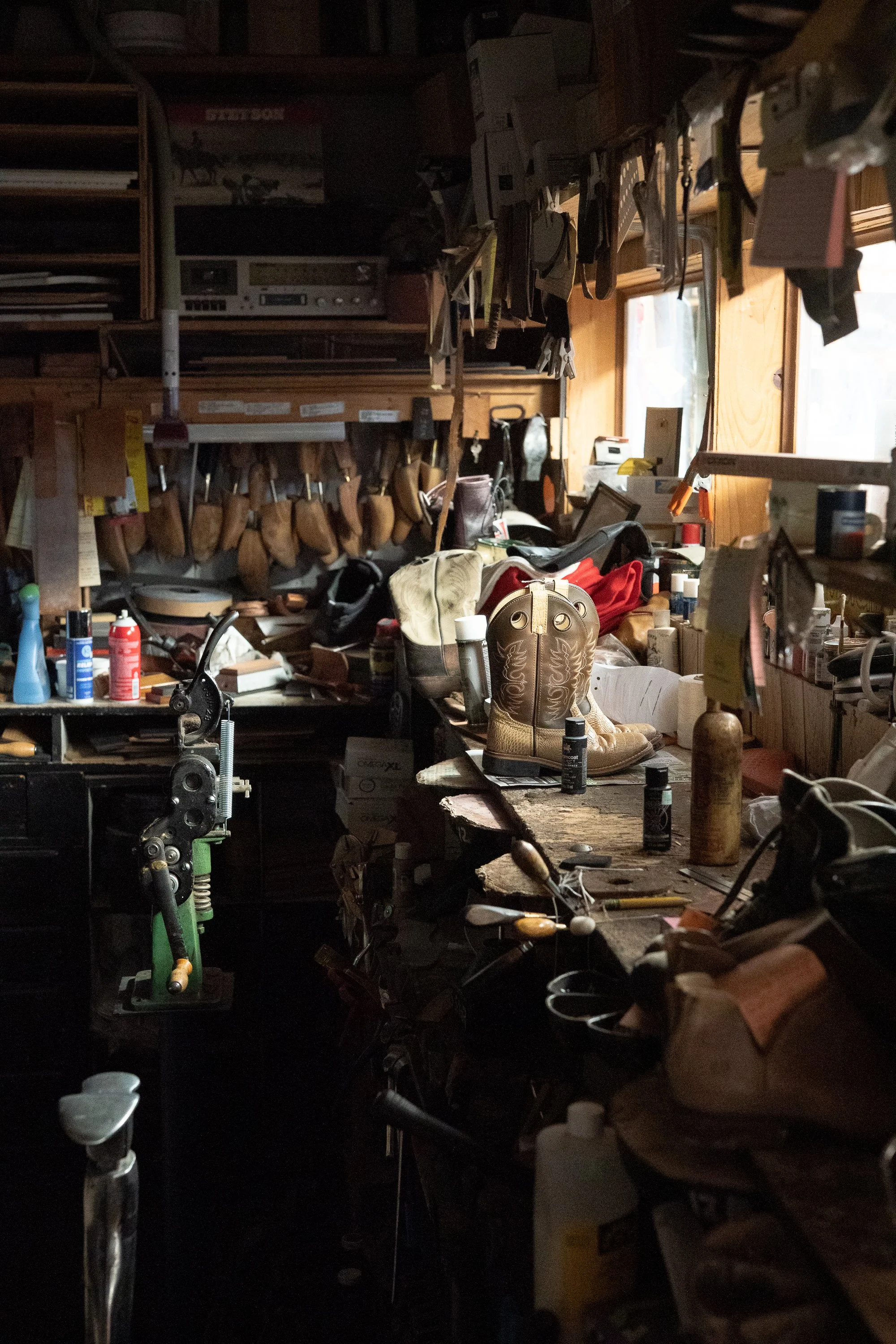 Embroidered cowboy boots, leatherworking supplies and repair equipment arranged across a workbench at City Shoe & Saddle Shop in Douglas, Wyoming.