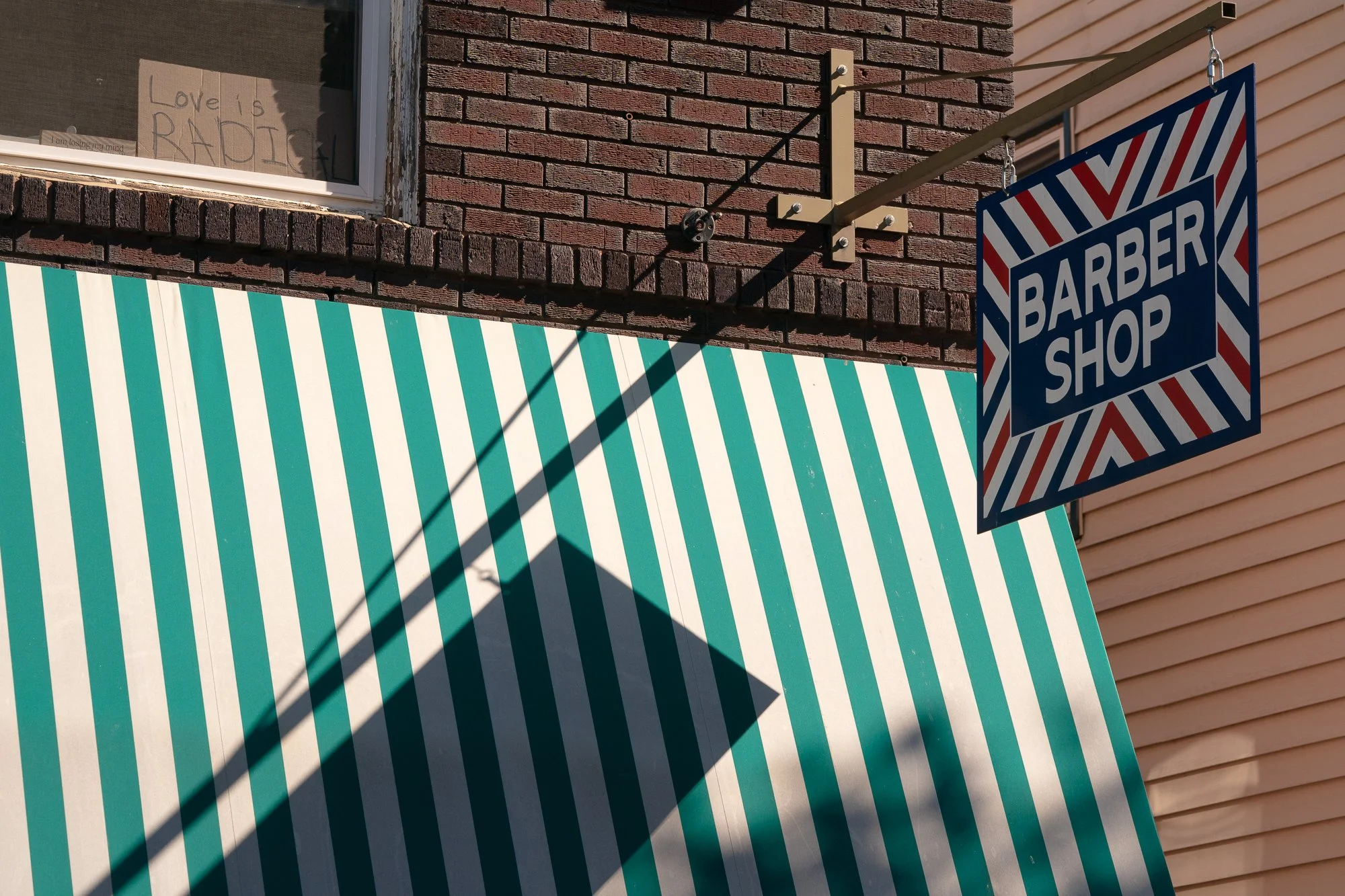 Classic barber shop sign hanging above a green striped awning on a brick storefront in Covington, Kentucky.