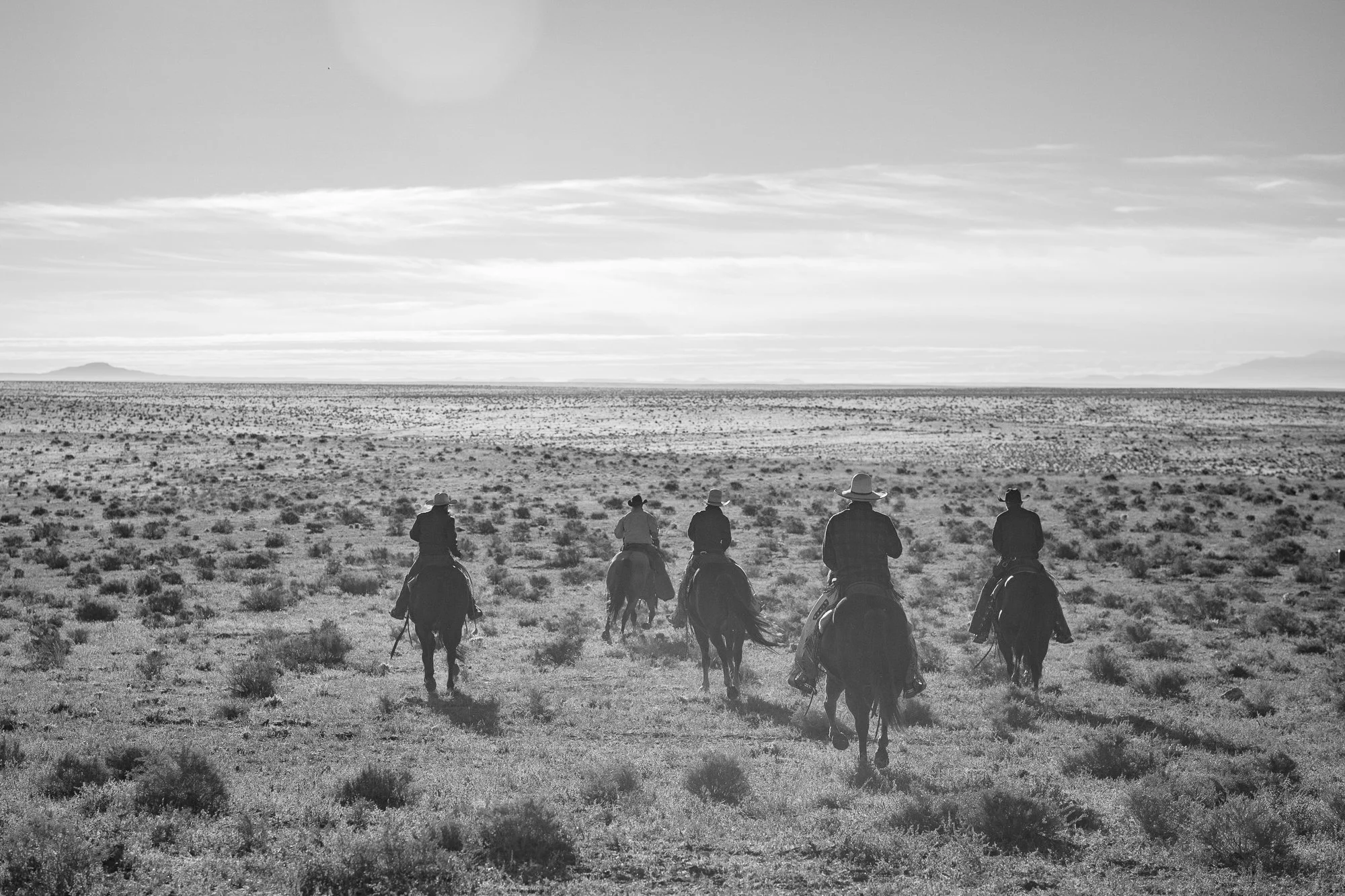 Group of cowboys riding across open range landscape at Diamond A Ranch Arizona under wide sky