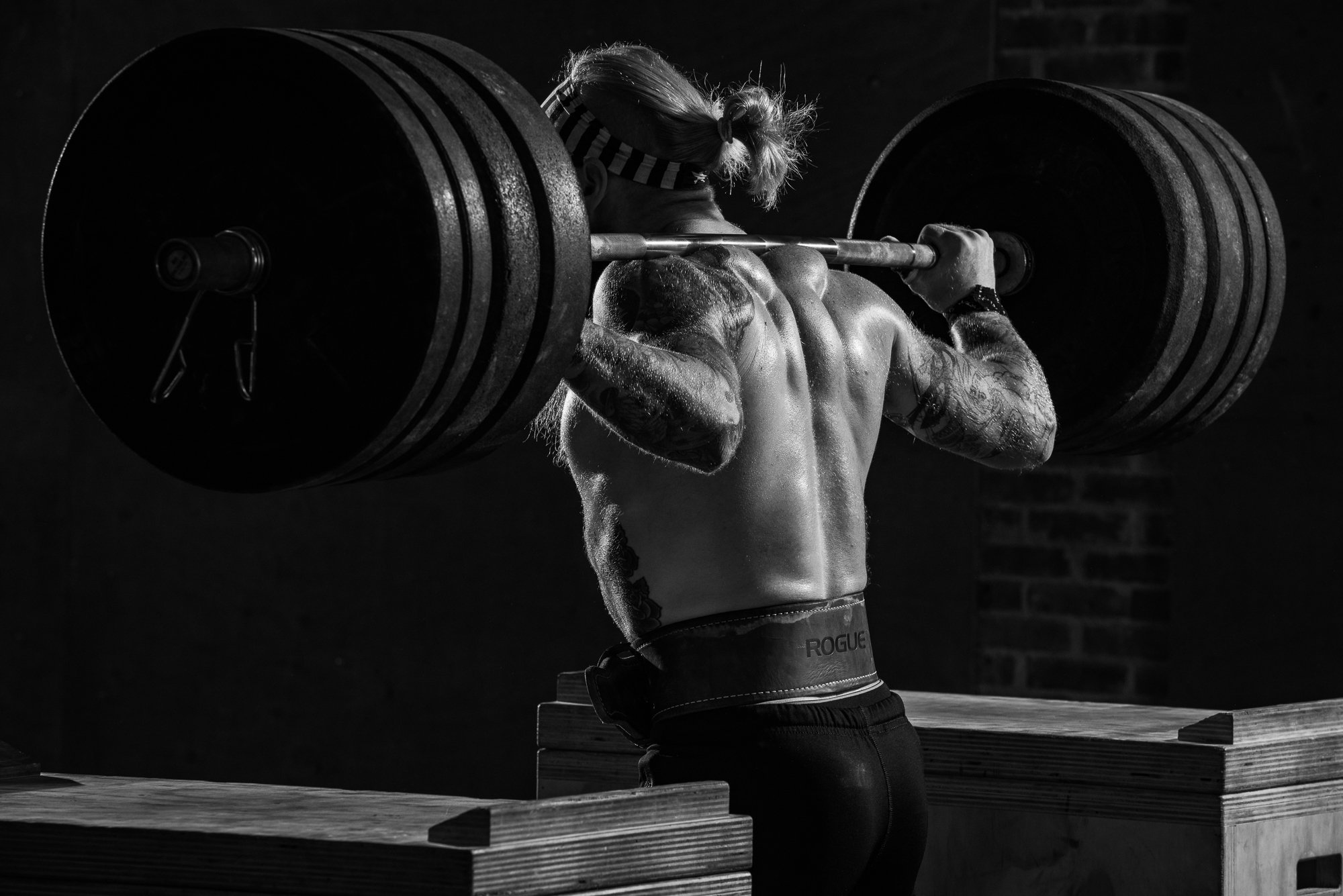Female CrossFit athlete holding a heavily loaded barbell across her shoulders between wooden plyometric boxes.