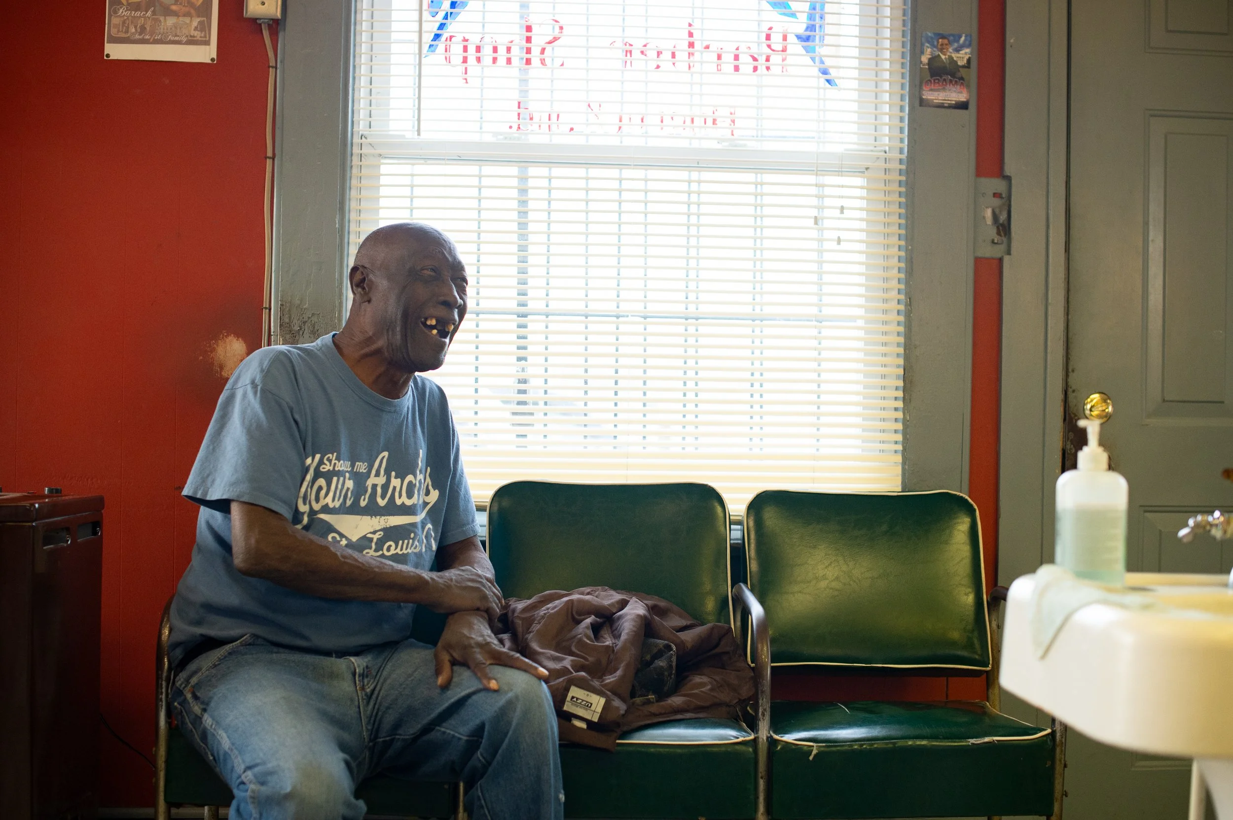 Man sitting and laughing on a chair near a window inside a barbershop in Maryland