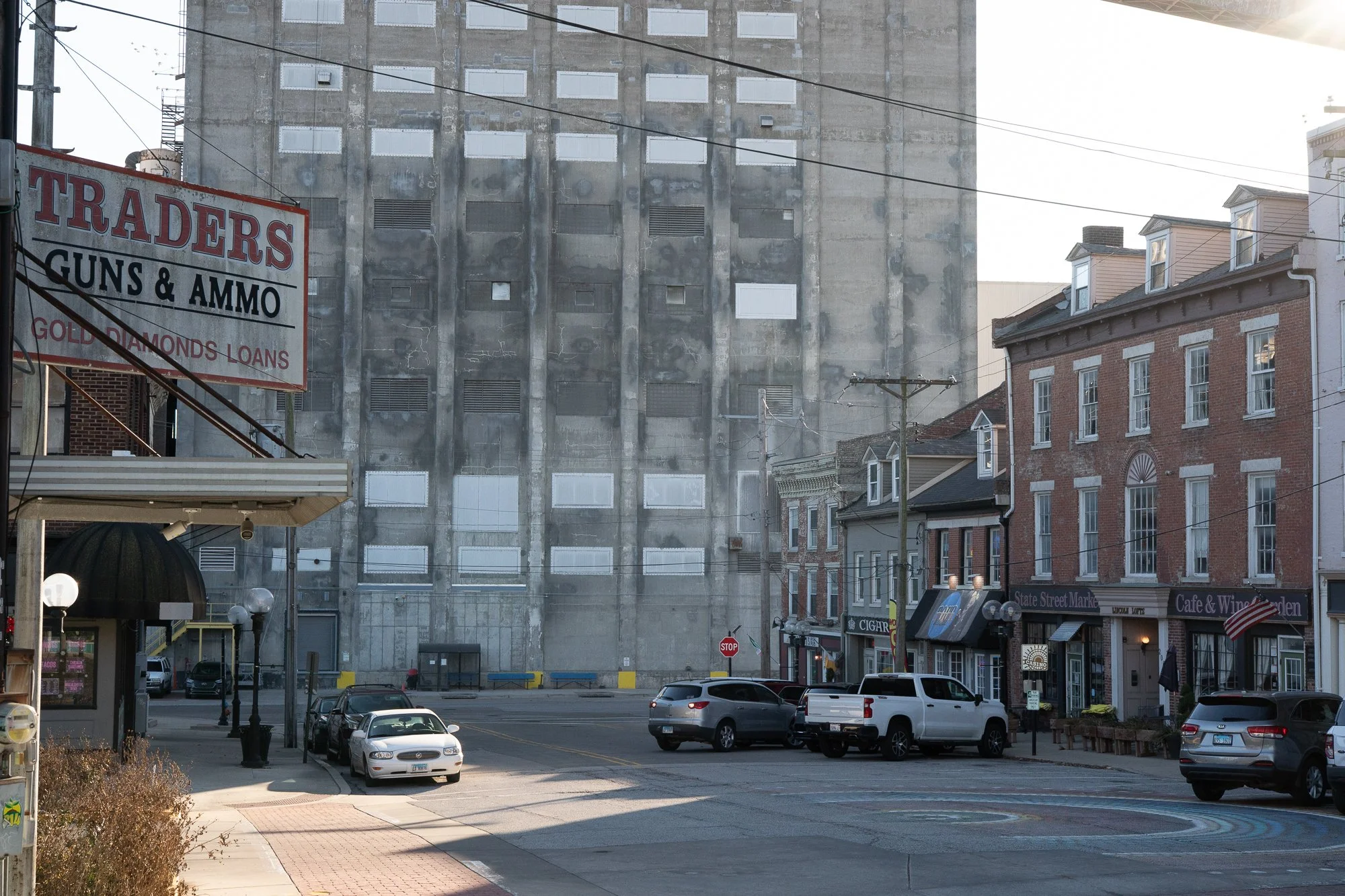Large industrial building behind a small town street with cars and storefronts in Alton, Illinois