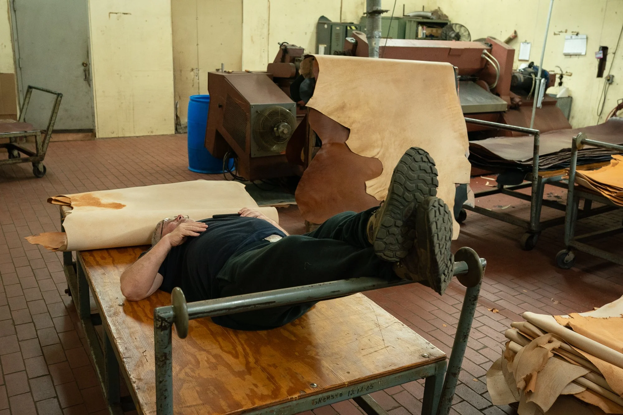 A worker lies on a work table surrounded by leather hides and processing equipment inside the Wickett & Craig tannery