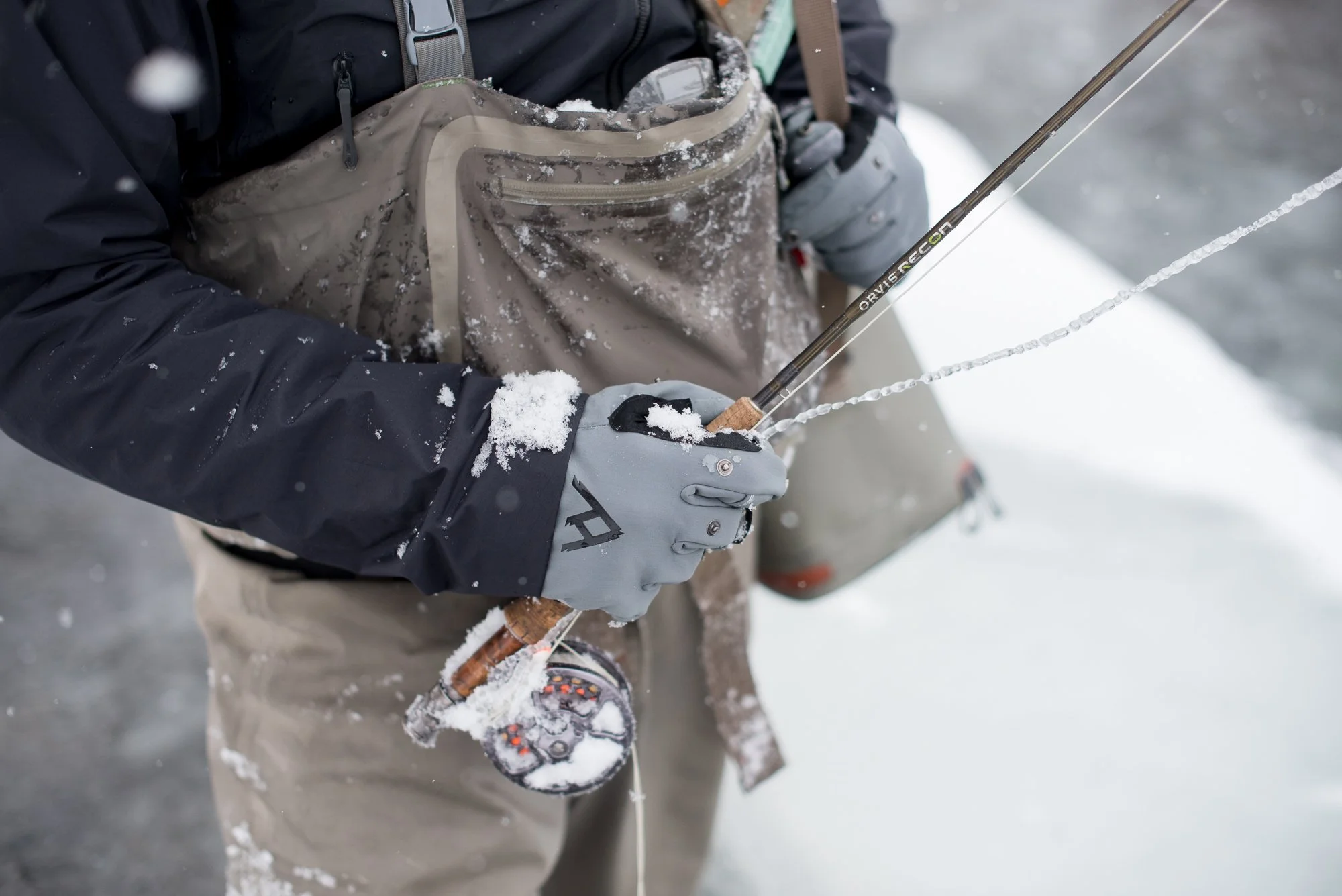 A close-up of gloved hands holding an iced fly fishing rod during winter on Clear Creek.