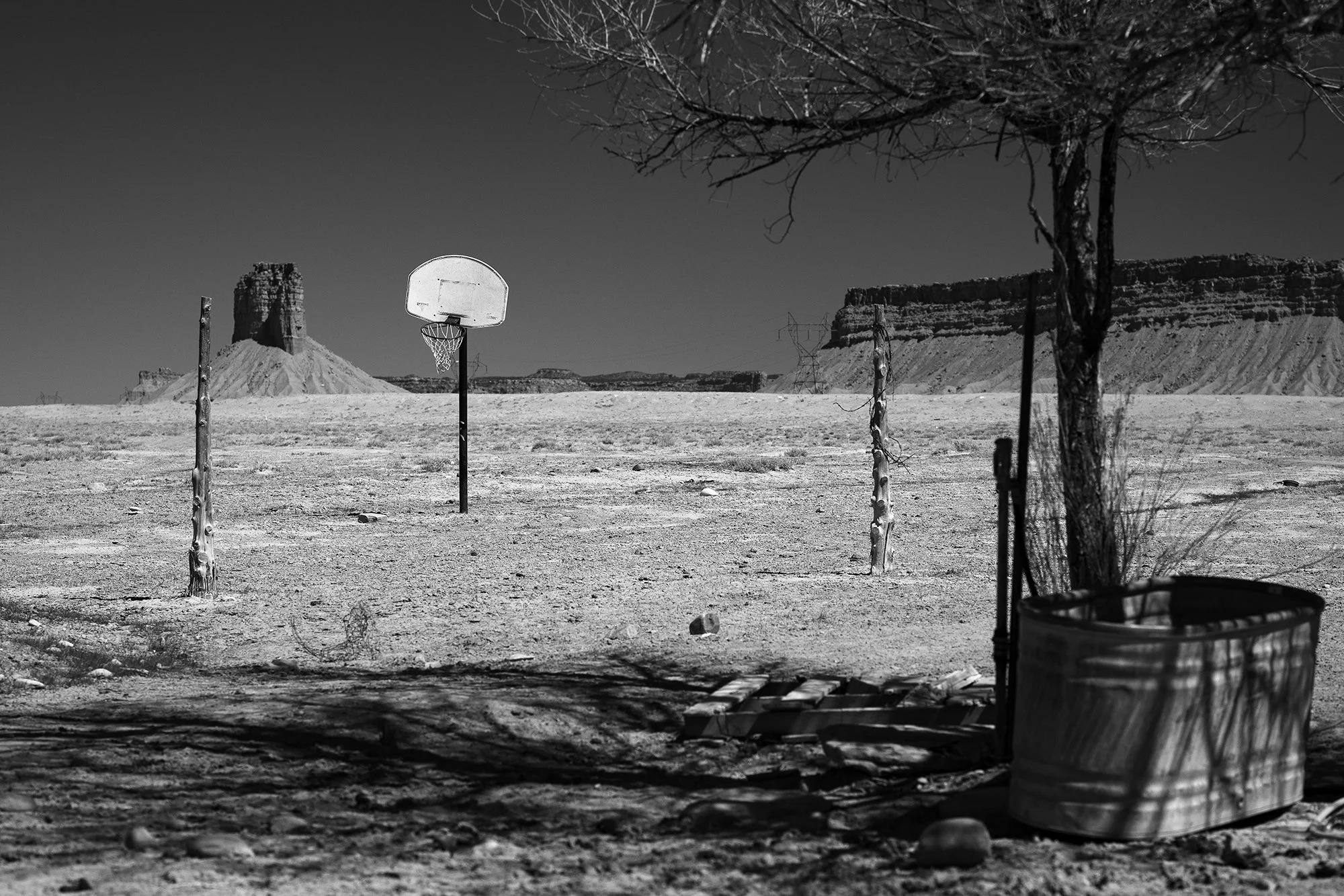Lone basketball hoop standing in an open landscape with rocky terrain and large earth formations in the distance.