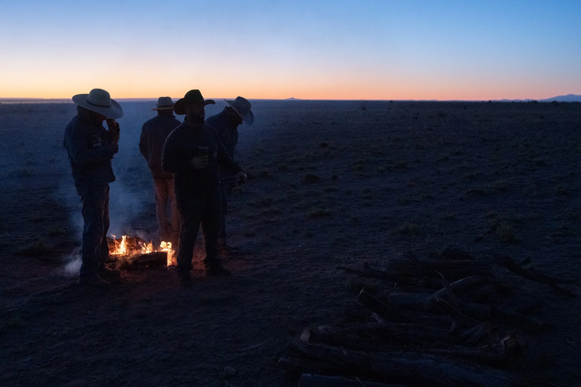 Cowboys standing near a small fire in low light on the Diamond A Ranch