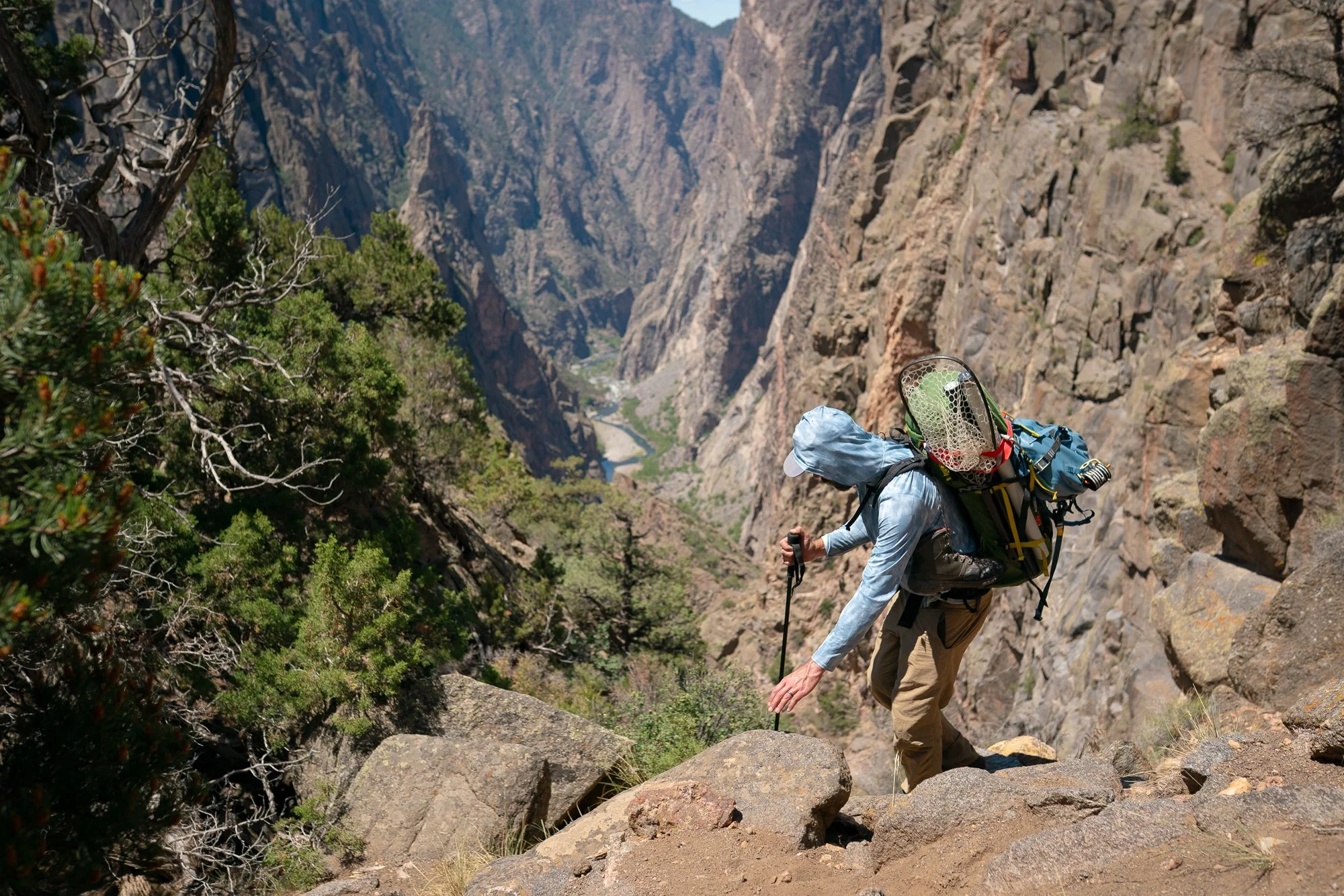 An angler hikes steep canyon terrain with fly fishing gear above Black Canyon of the Gunnison