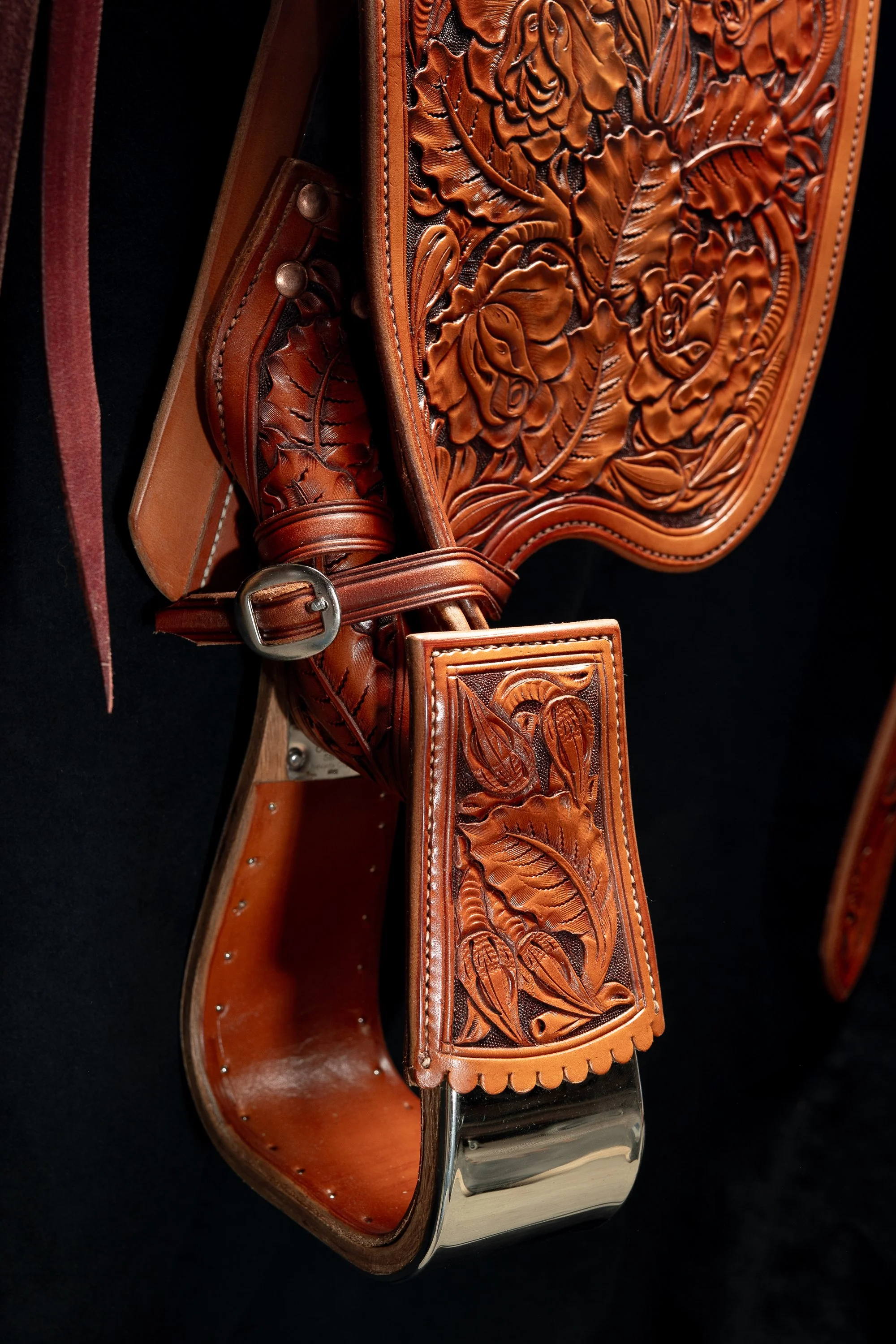 Leather tooling, buckled strap and metal stirrup on a Mother Hubbard saddle.