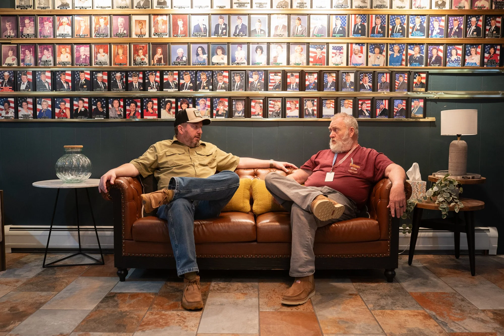 Veterans seated on a leather couch beneath rows of portraits inside a VFW hall