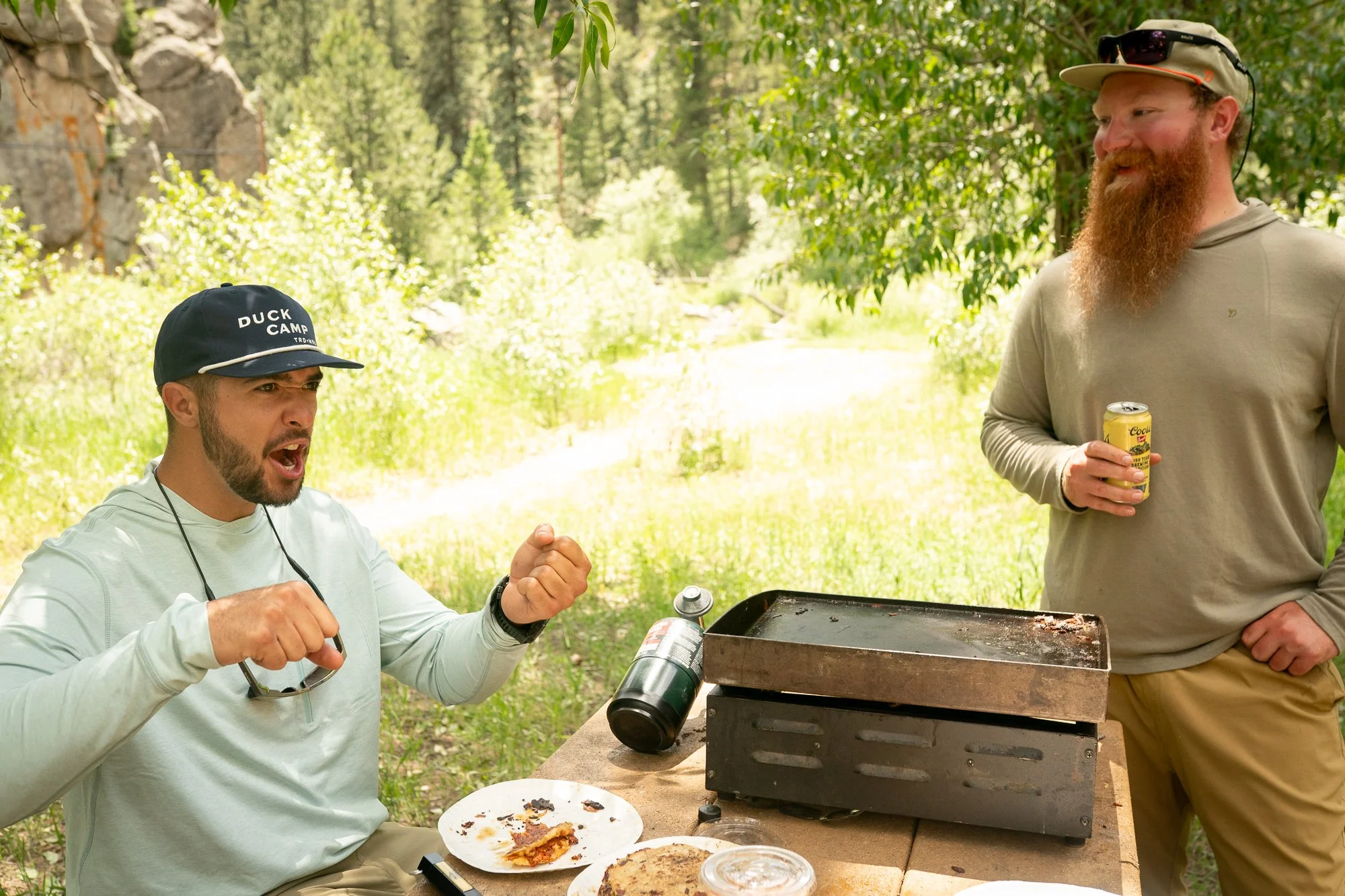 Two anglers stand by a camp stove and lunch table during a riverside break from a Duck Camp fly fishing shoot