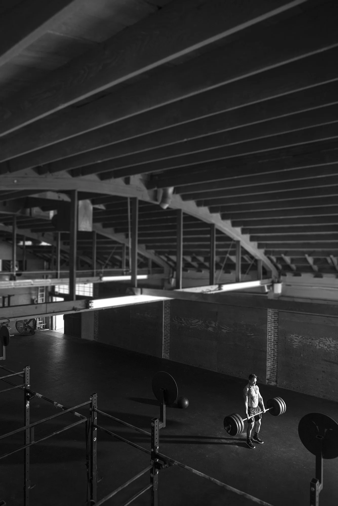 black and white wide shot of athlete lifting barbell alone in large gym space