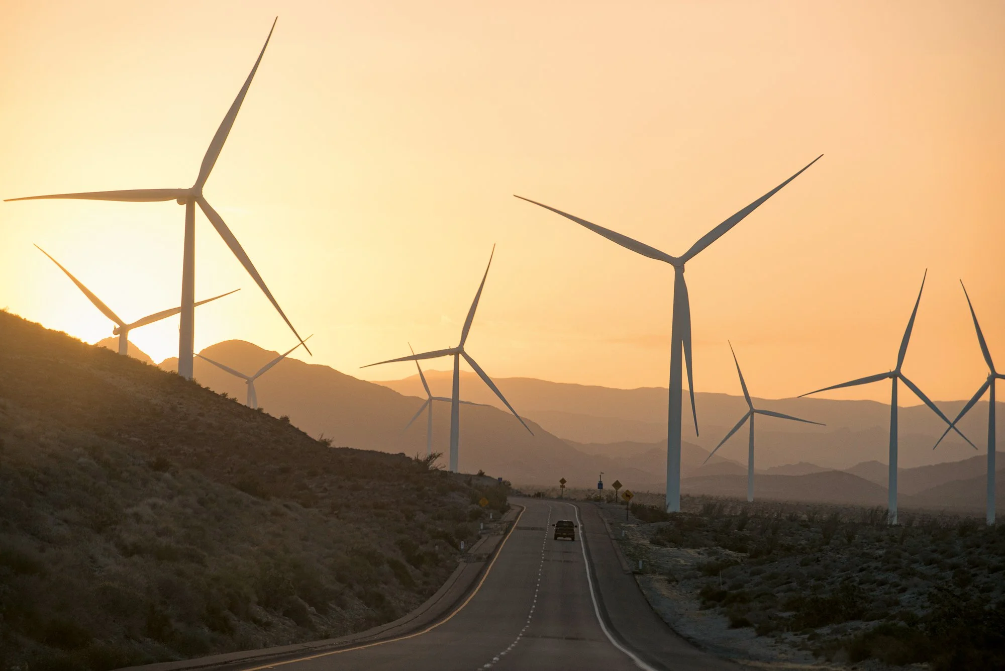 Wind turbines lining desert highway at sunset with warm light and long shadows