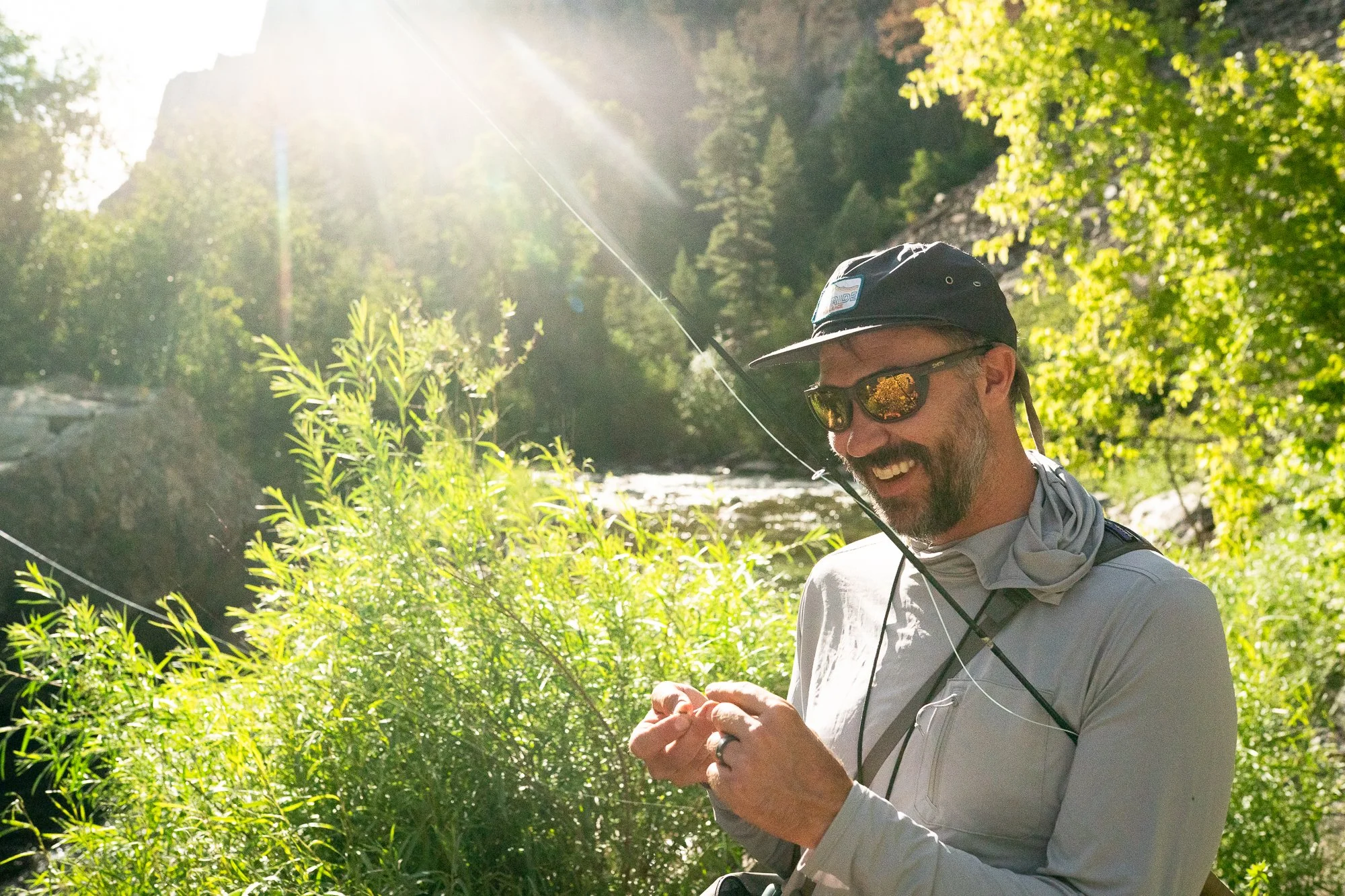 A fly angler smiles while working with line near the river in bright afternoon light