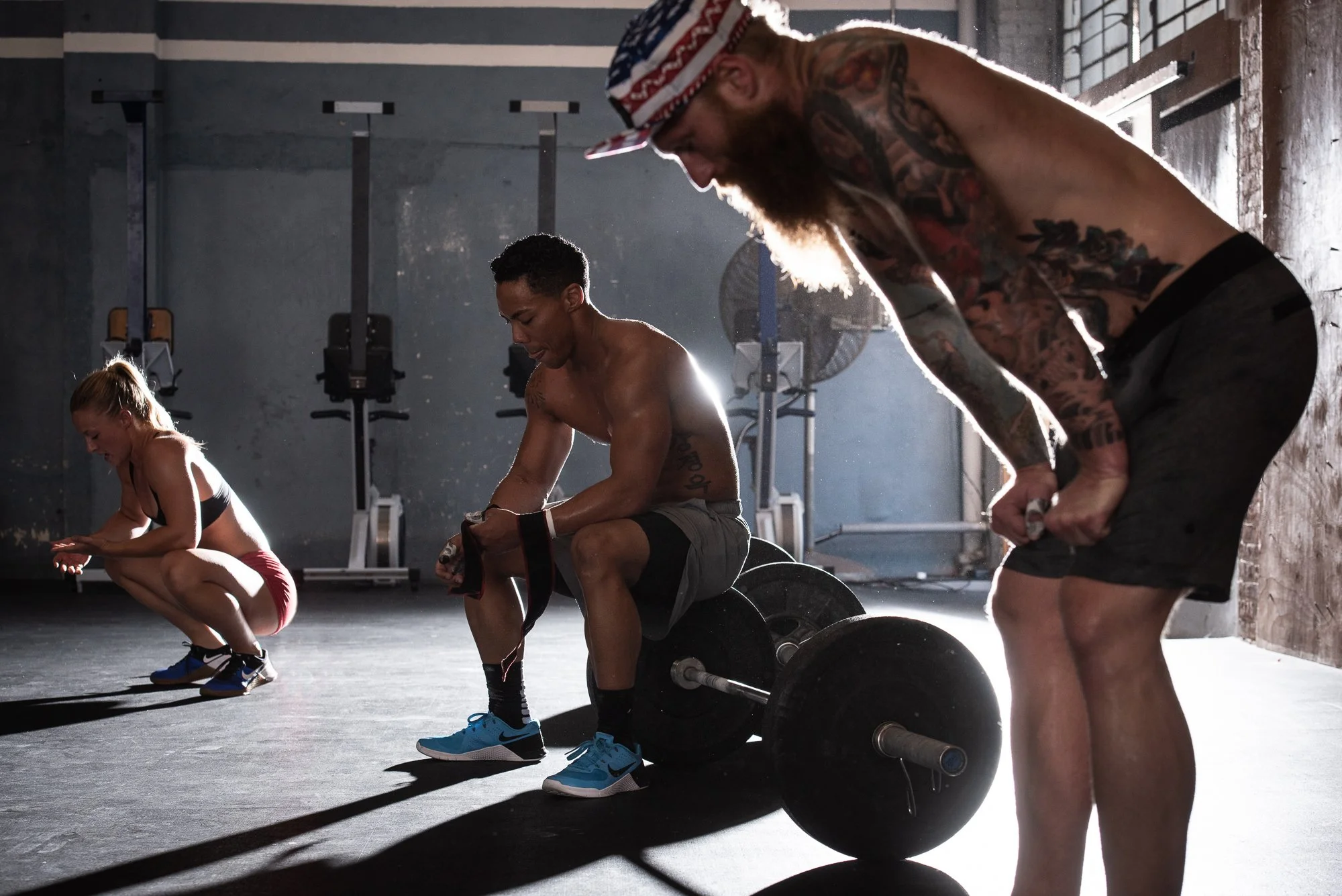 CrossFit athletes resting beside loaded barbells between training efforts.