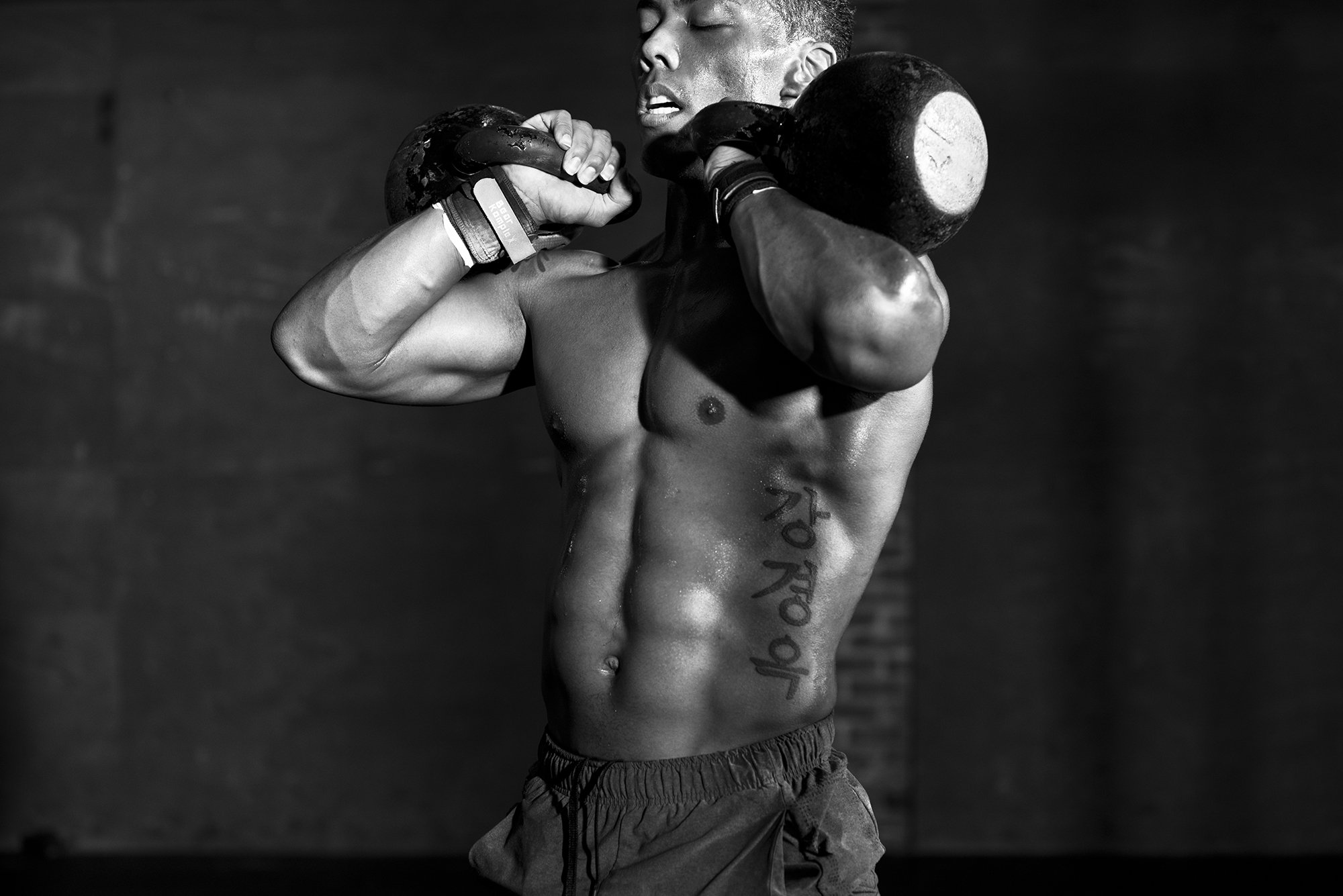 black and white image of male athlete lifting kettlebells during strength training