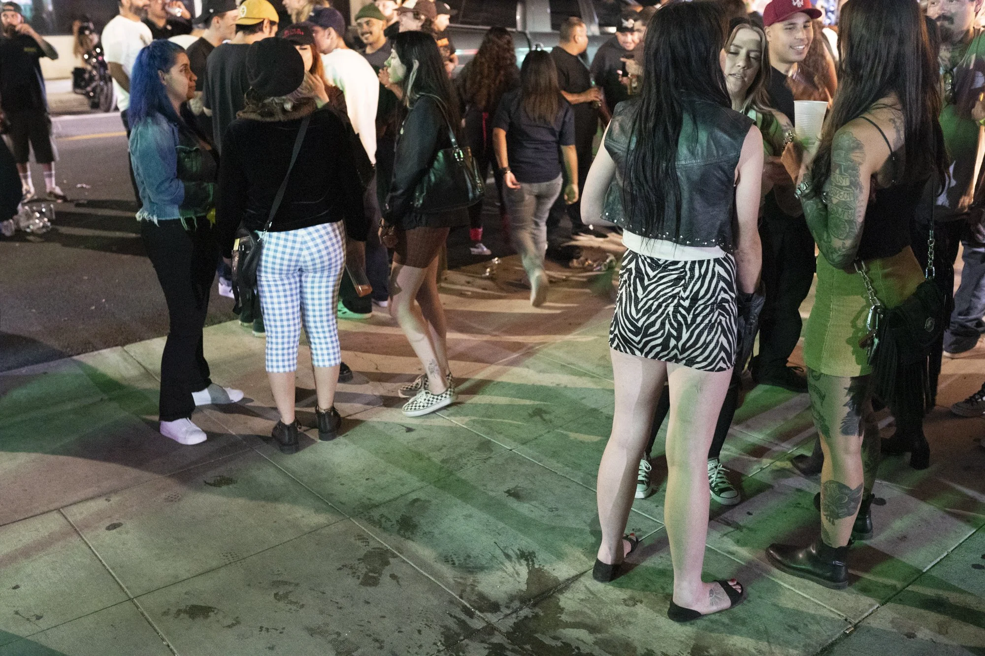 Groups of people standing and talking on a Long Beach sidewalk at night during a crowded street event