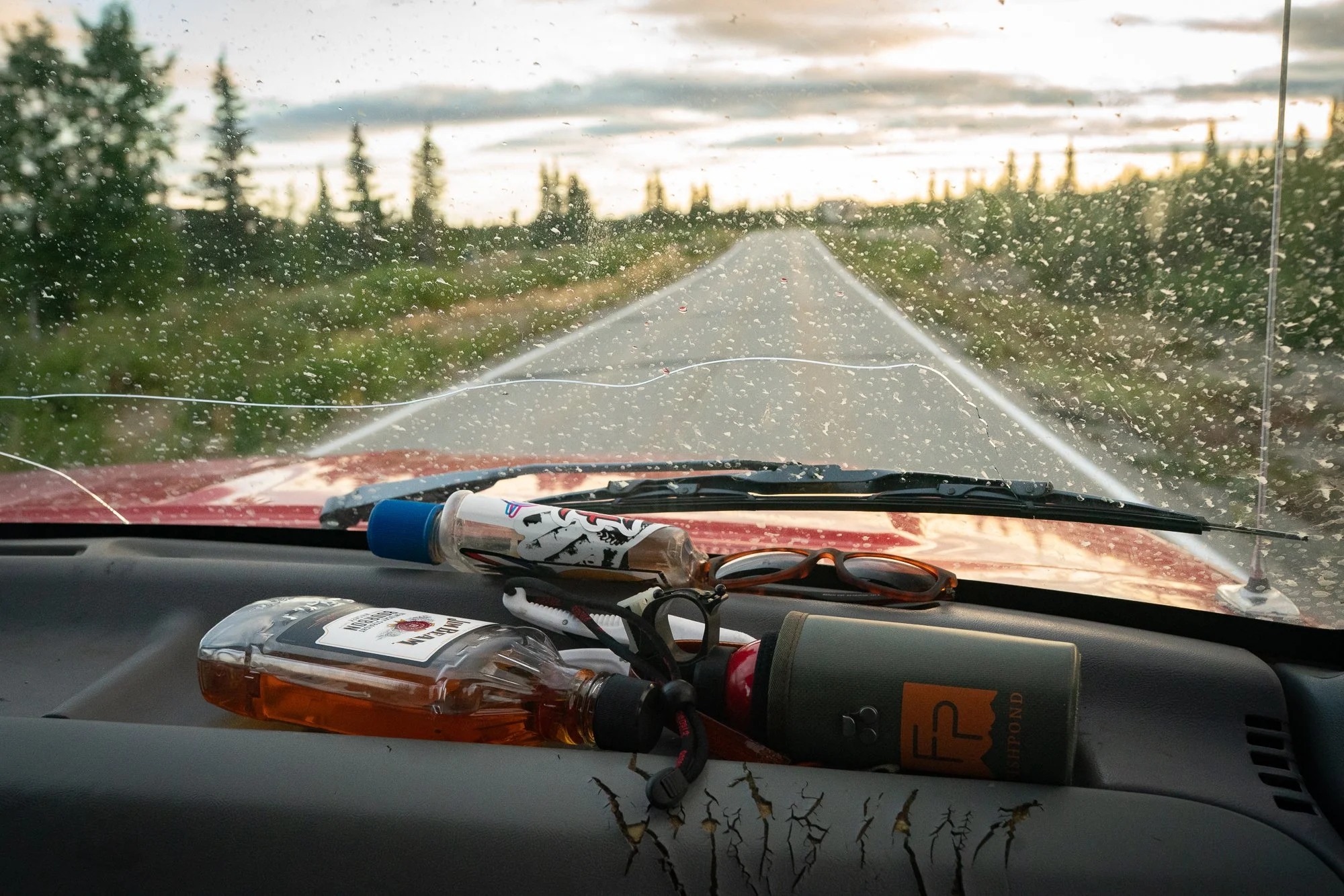 Truck dashboard with fishing gear and bottles on a wet road in Alaska