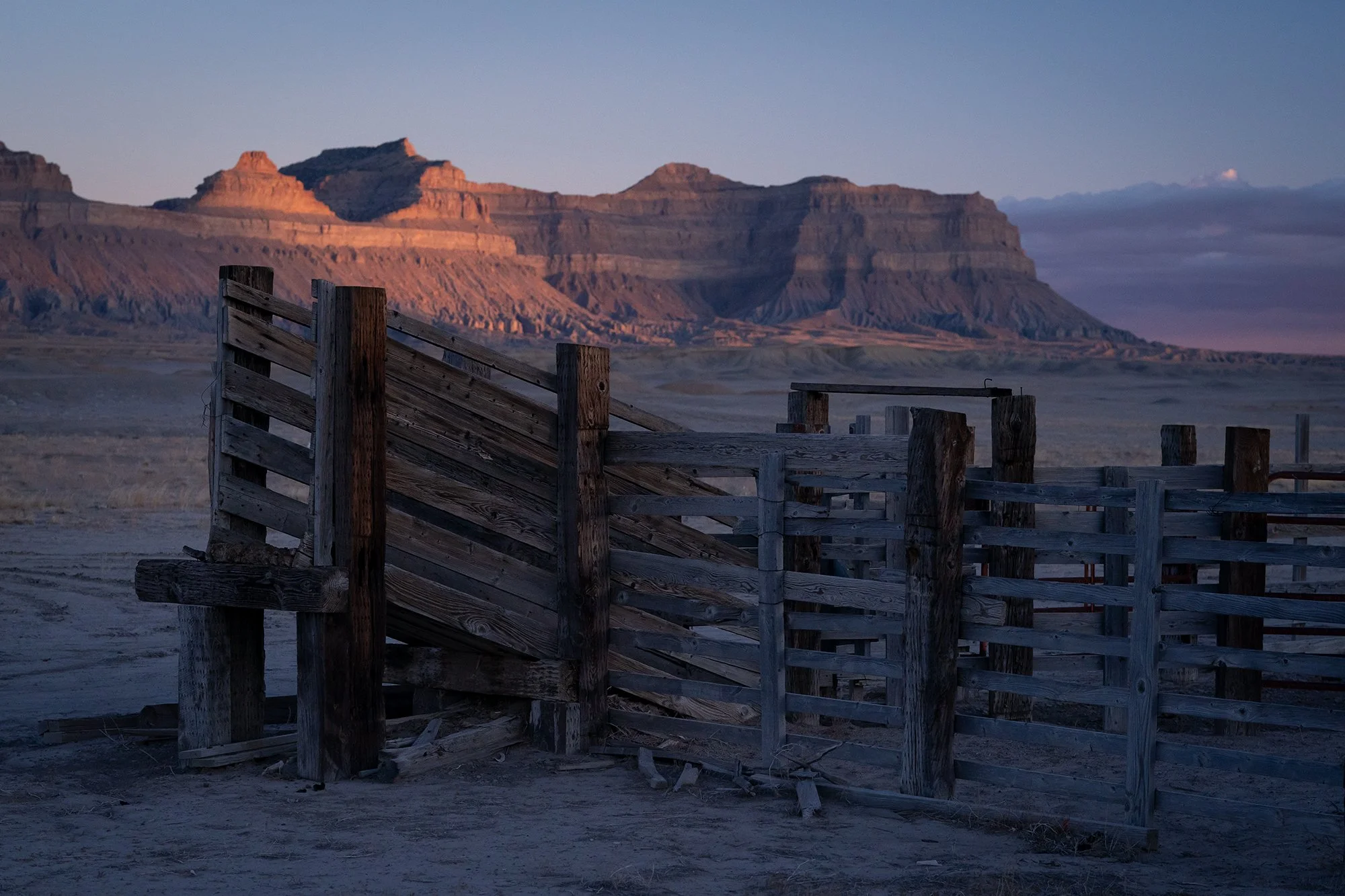 A wooden cattle corral in an open desert landscape with mesas in the background, suited for western landscape wall art and nature photography prints
