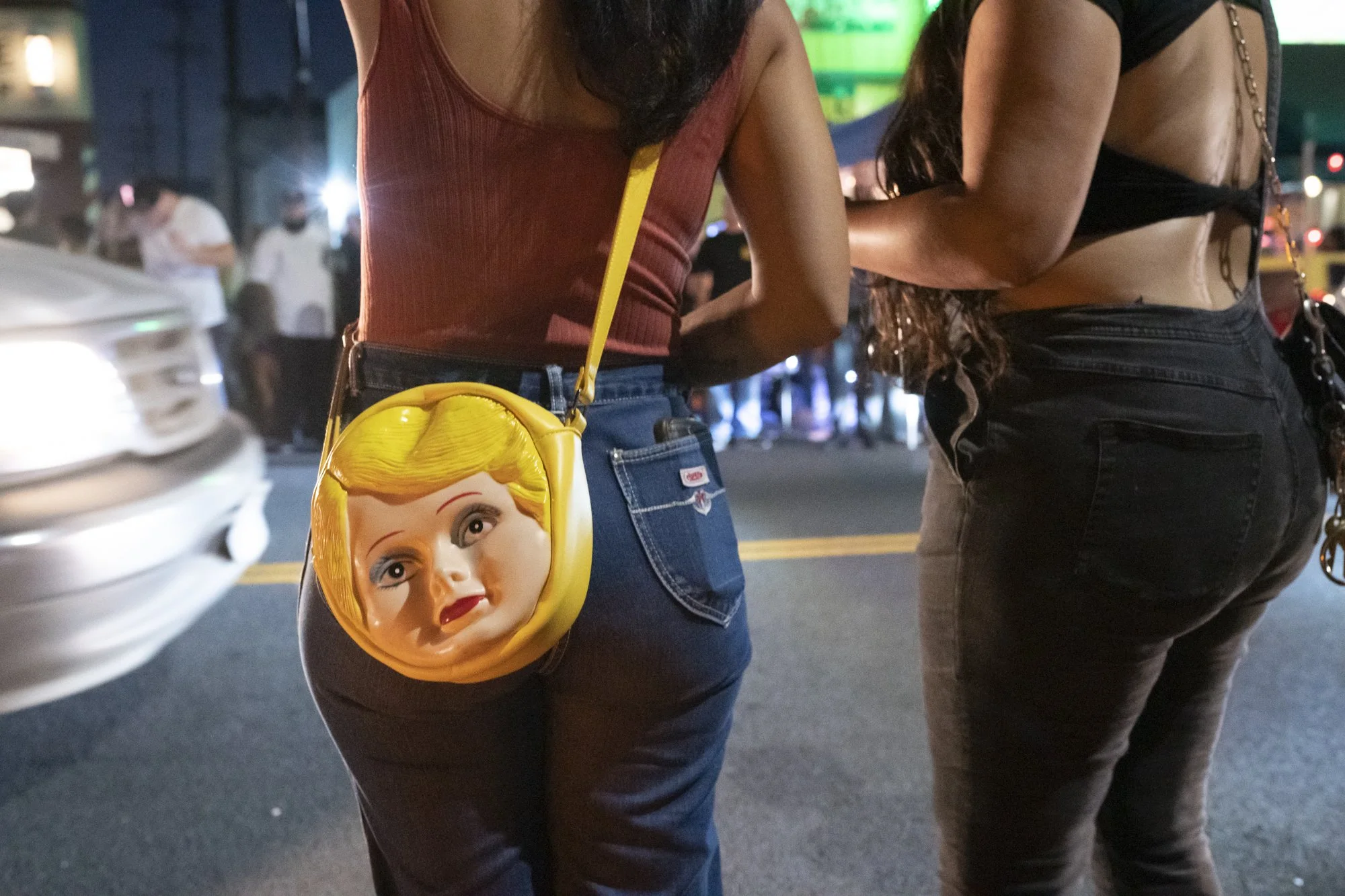 Close-up of a woman wearing a doll-face novelty purse on a Long Beach street at night during the Syndicate Barbershop anniversary event