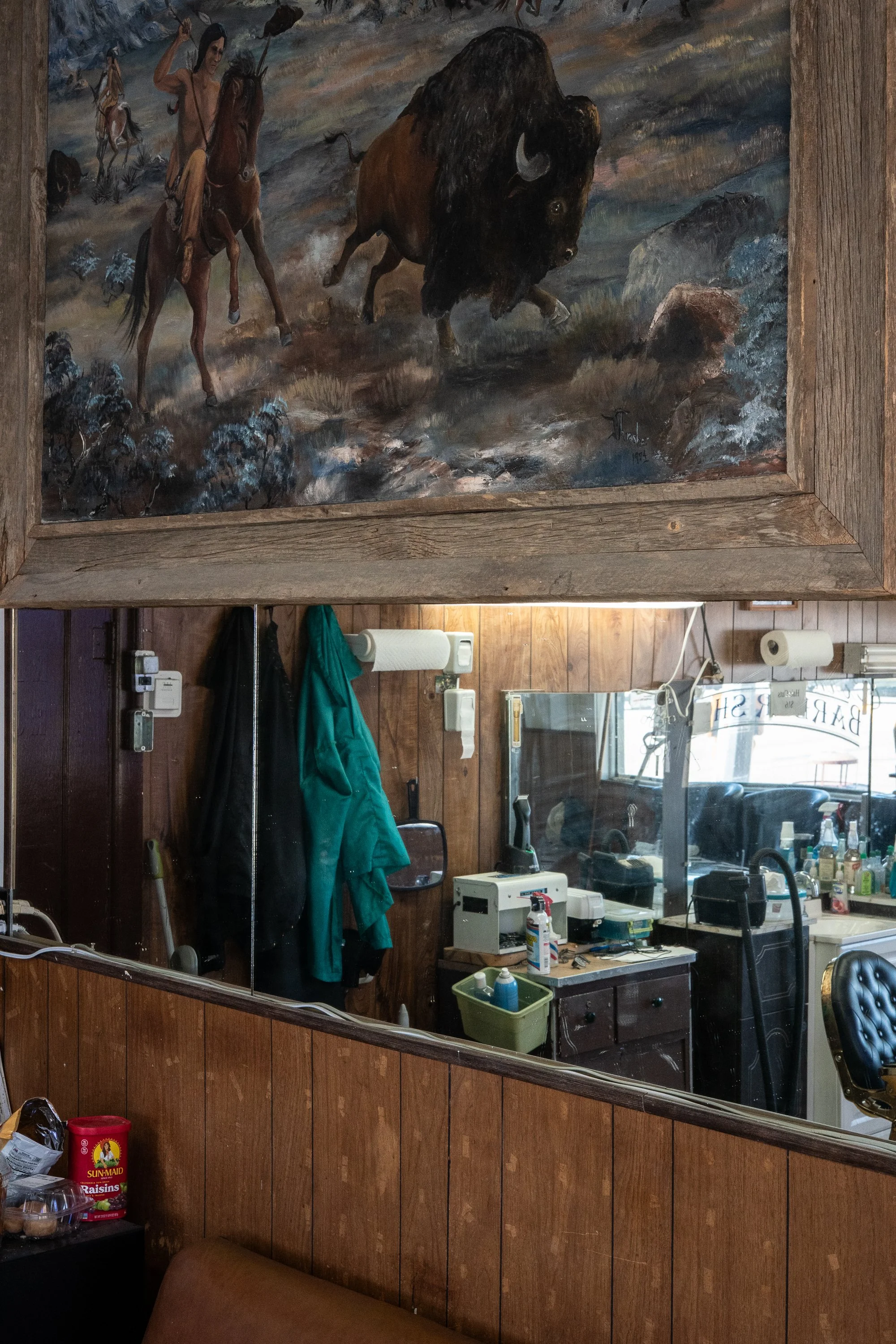 Corner Barbershop interior in Douglas, Wyoming, with barber chairs, mirrors, wooden wall paneling and a framed Western painting above the stations.