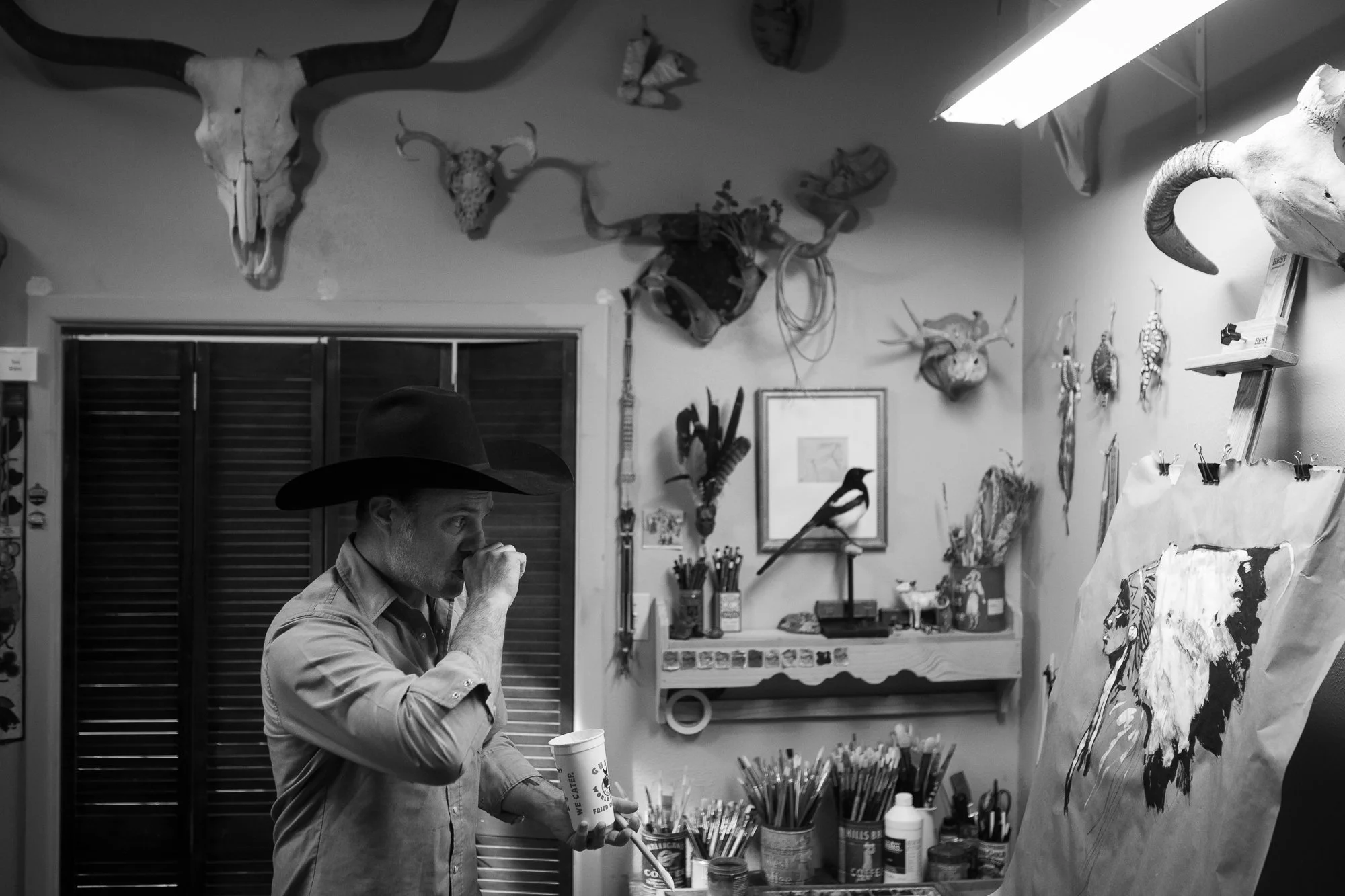 Black and white photograph of Teal Blake reflecting in his art studio surrounded by Western artifacts