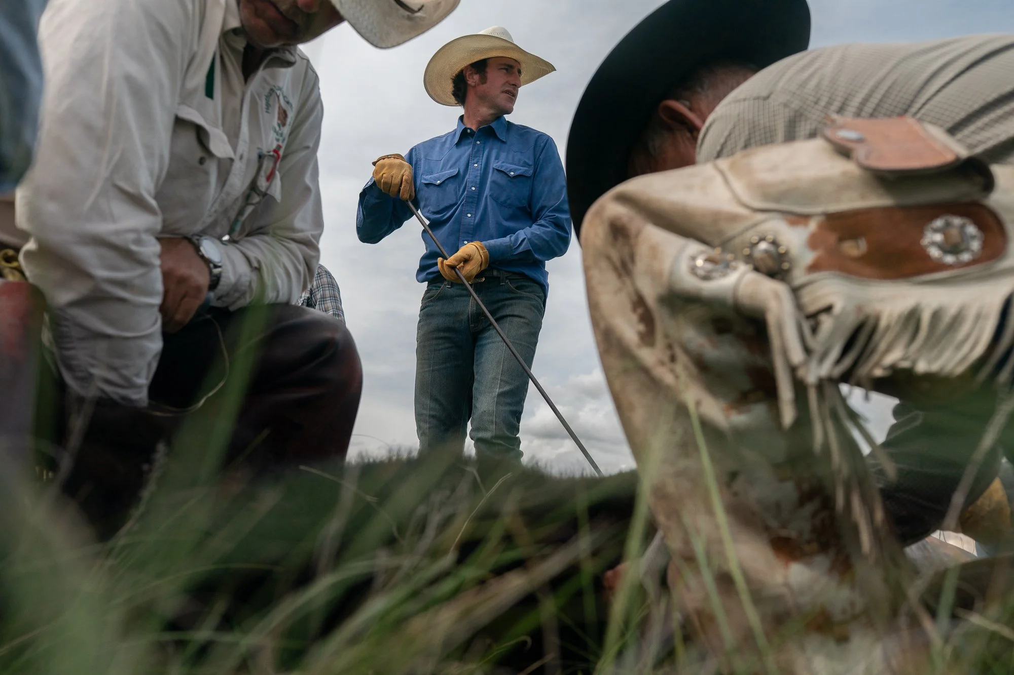 Low-angle view of cowboys branding calves in the grass at Haythorn Ranch in the Nebraska Sandhills, with one cowboy standing holding a branding iron.