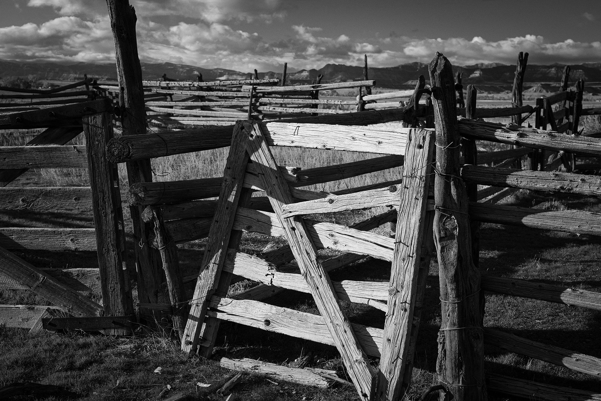 Black and white photograph of a weathered wooden cattle corral in the American West