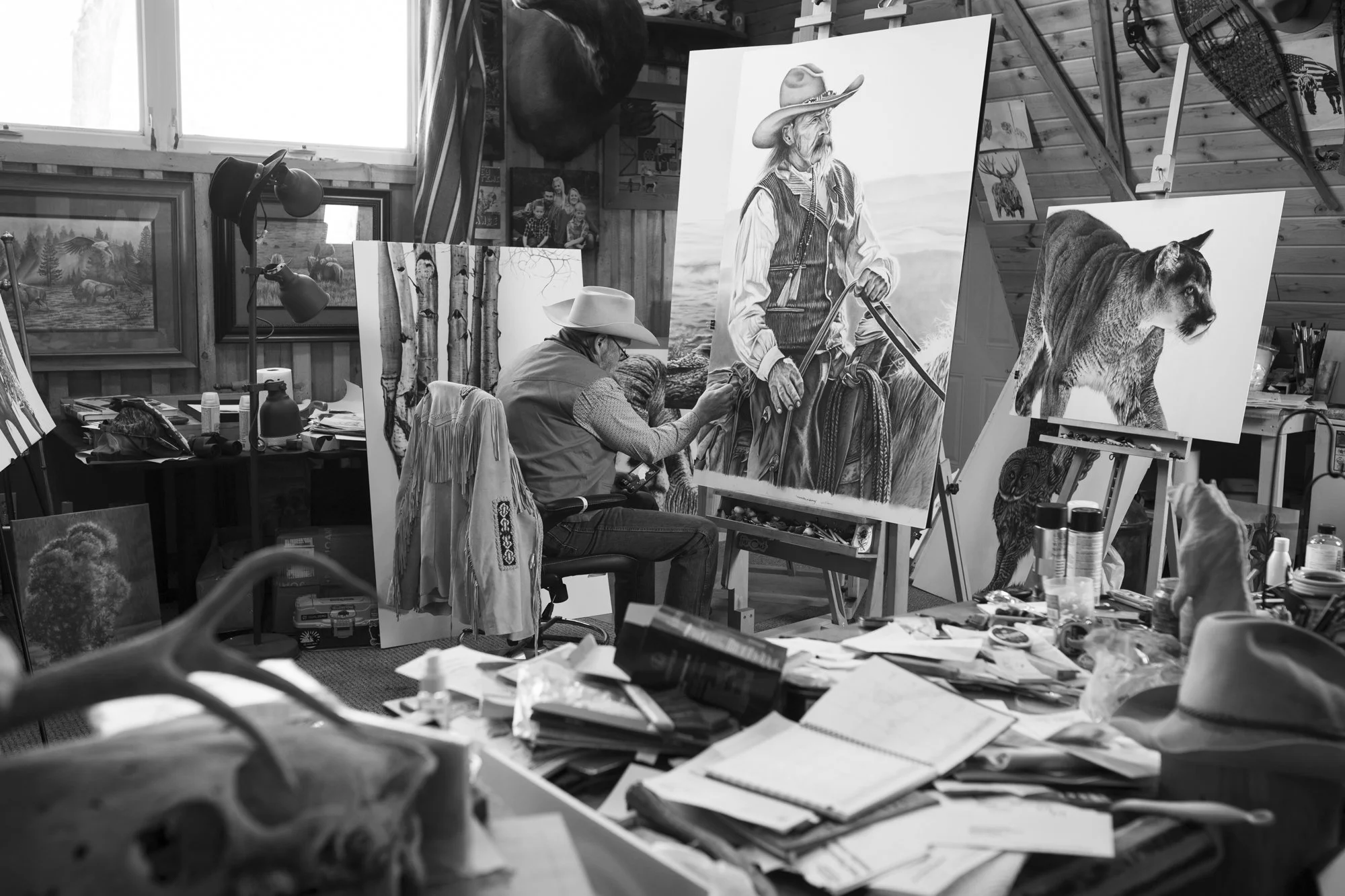 Black and white photograph of a Western artist in his studio surrounded by drawings and art supplies