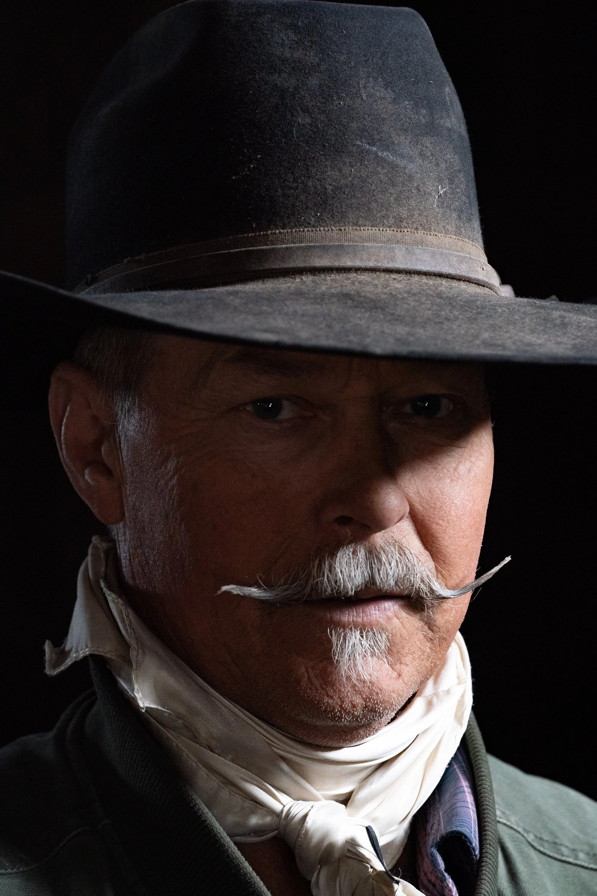Portrait of a cowboy wearing a dark hat and neck scarf during a documentary photography project