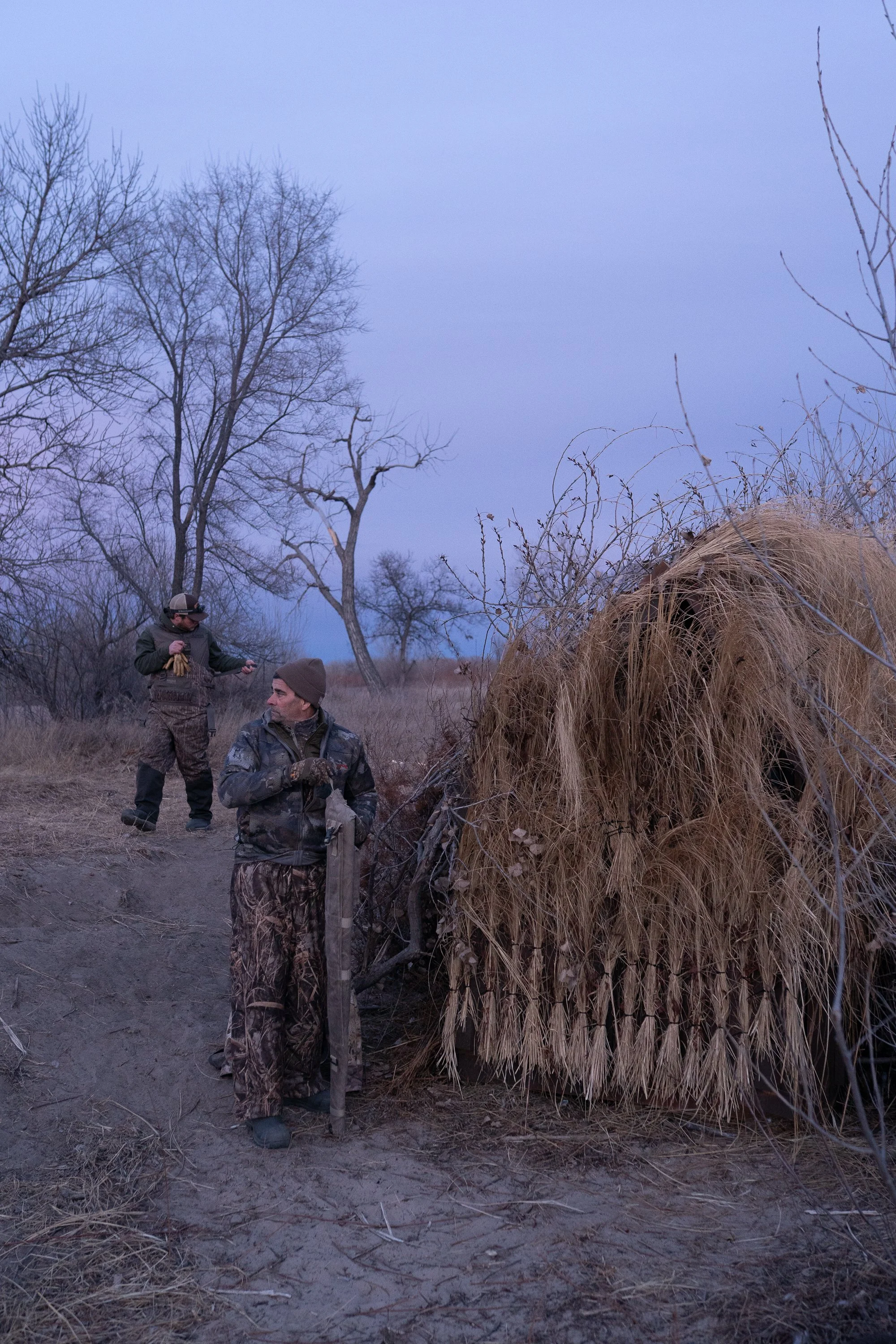 Duck hunters stand beside a camouflaged blind before sunrise