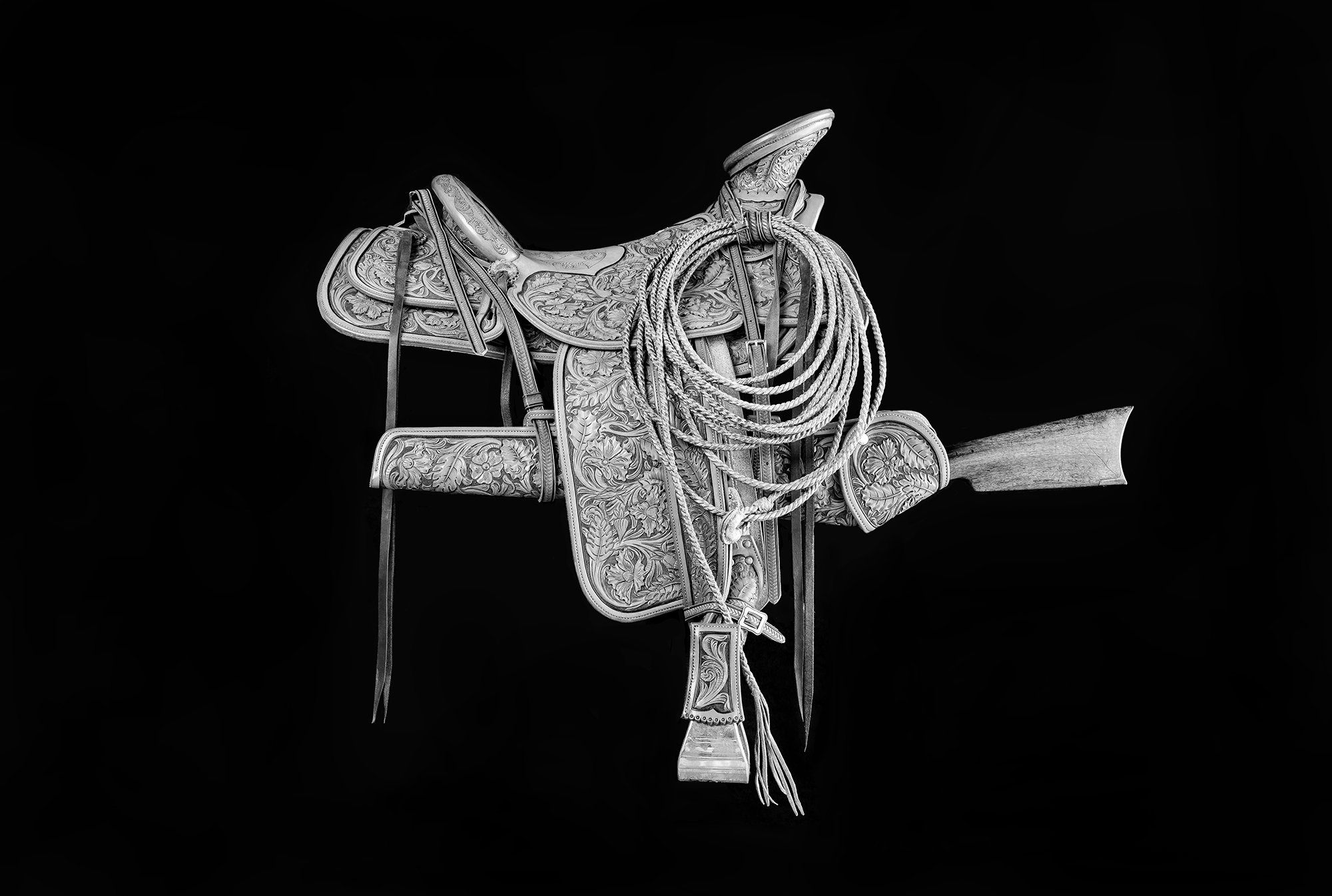 Black and white photograph of a beautiful custom Western saddle with a rifle and scabbard
