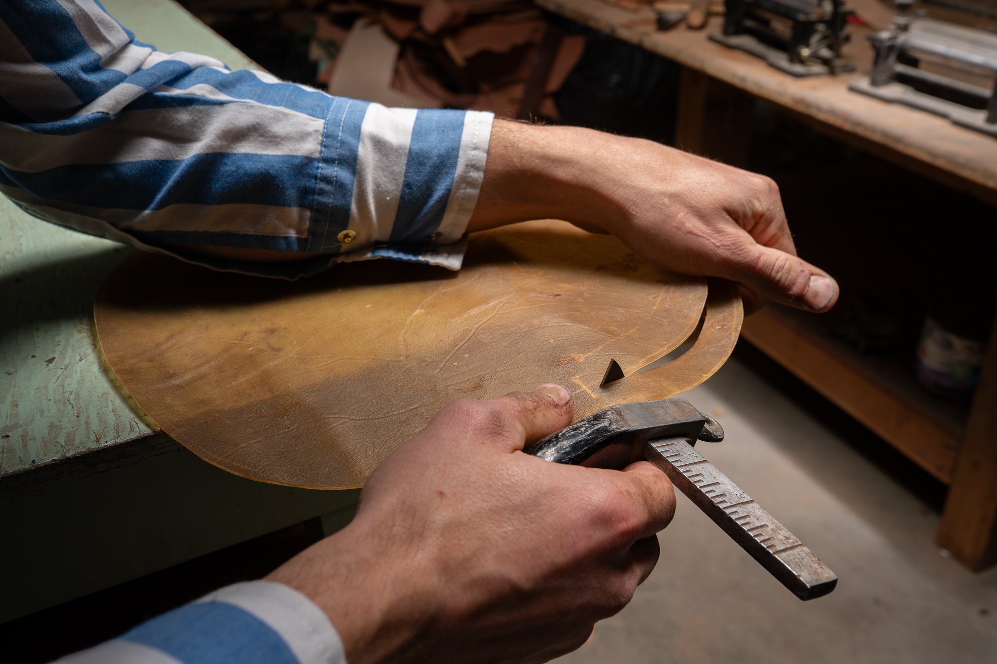 Hands cutting a prepared rawhide hide into long continuous strands using a traditional cutting tool