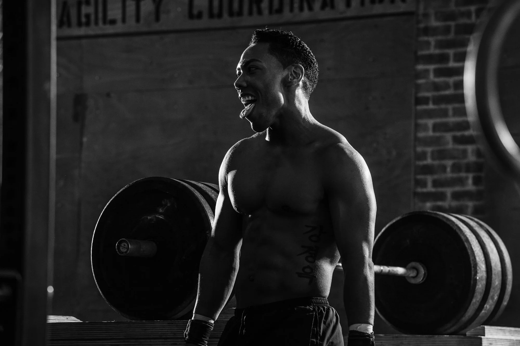 CrossFit athlete standing beside a loaded barbell in a gritty warehouse gym.