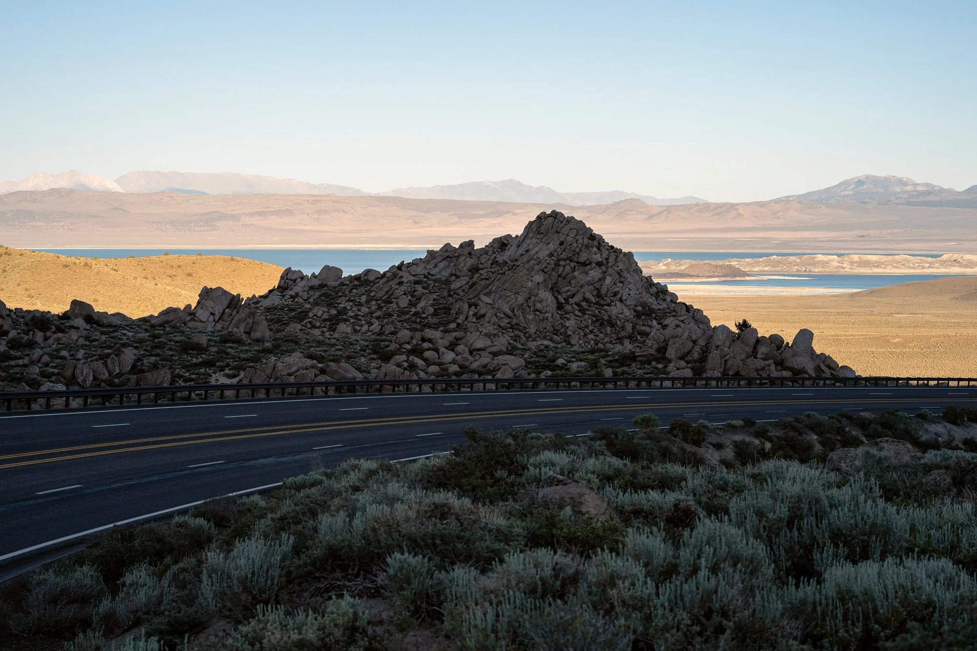 Desert highway passing rocky hill with expansive basin and distant mountains