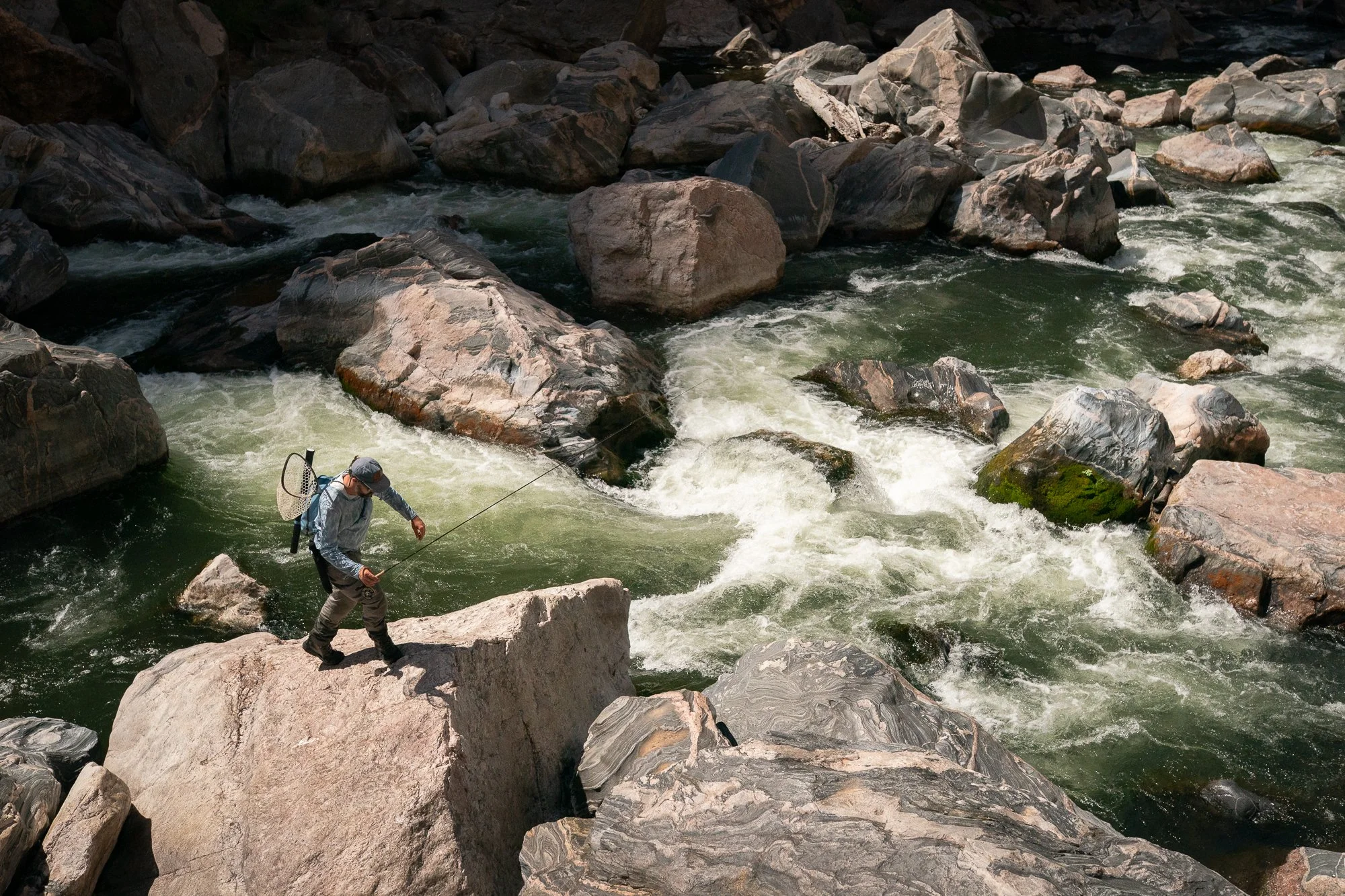 A fly angler stands on massive canyon boulders above fast-moving Gunnison River water