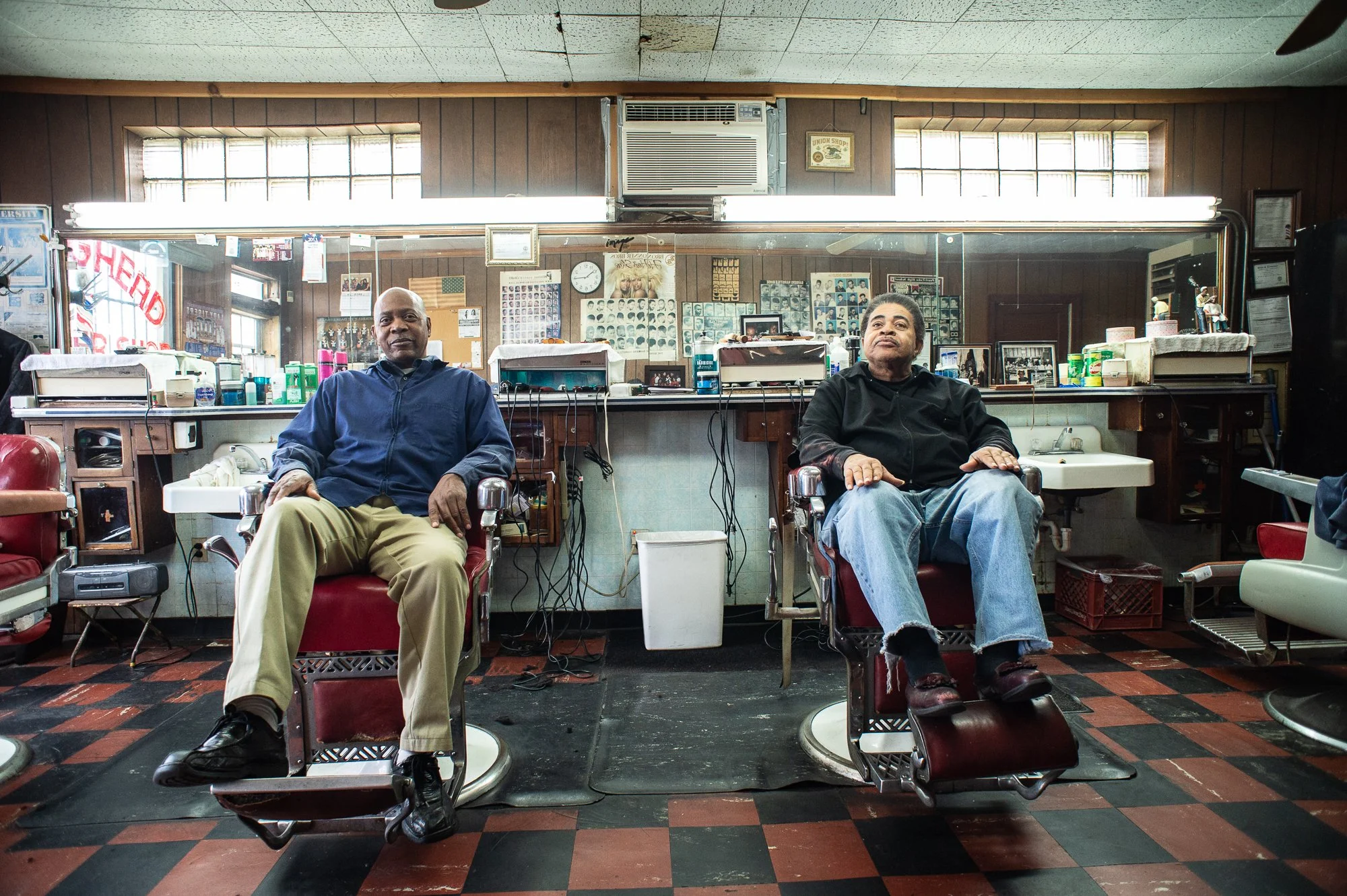 Two men seated in barber chairs inside a historic Black barbershop interior