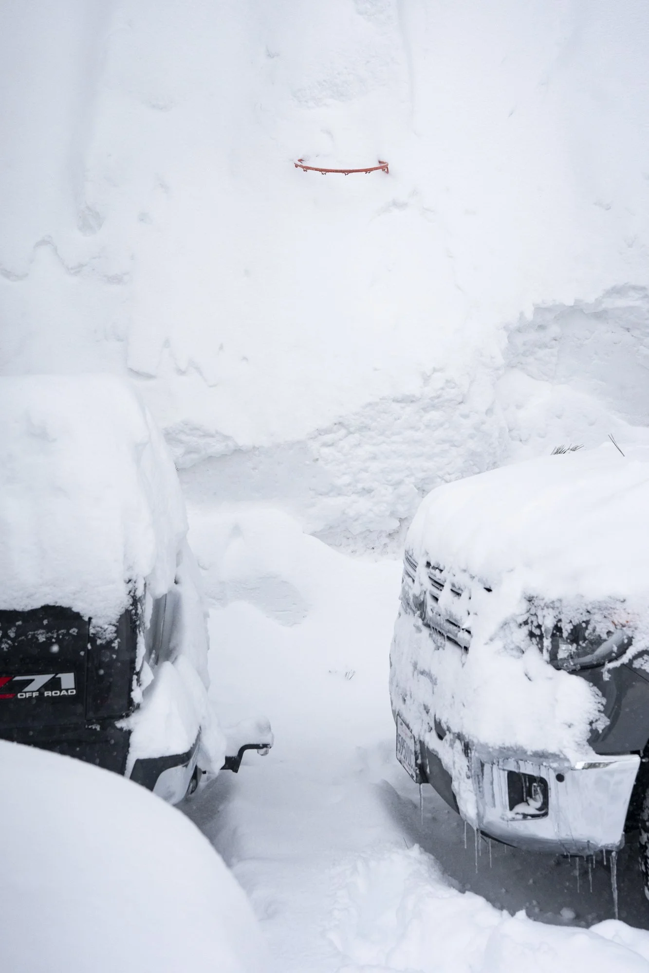 An orange basketball rim sticks out of a massive snow bank after a winter storm