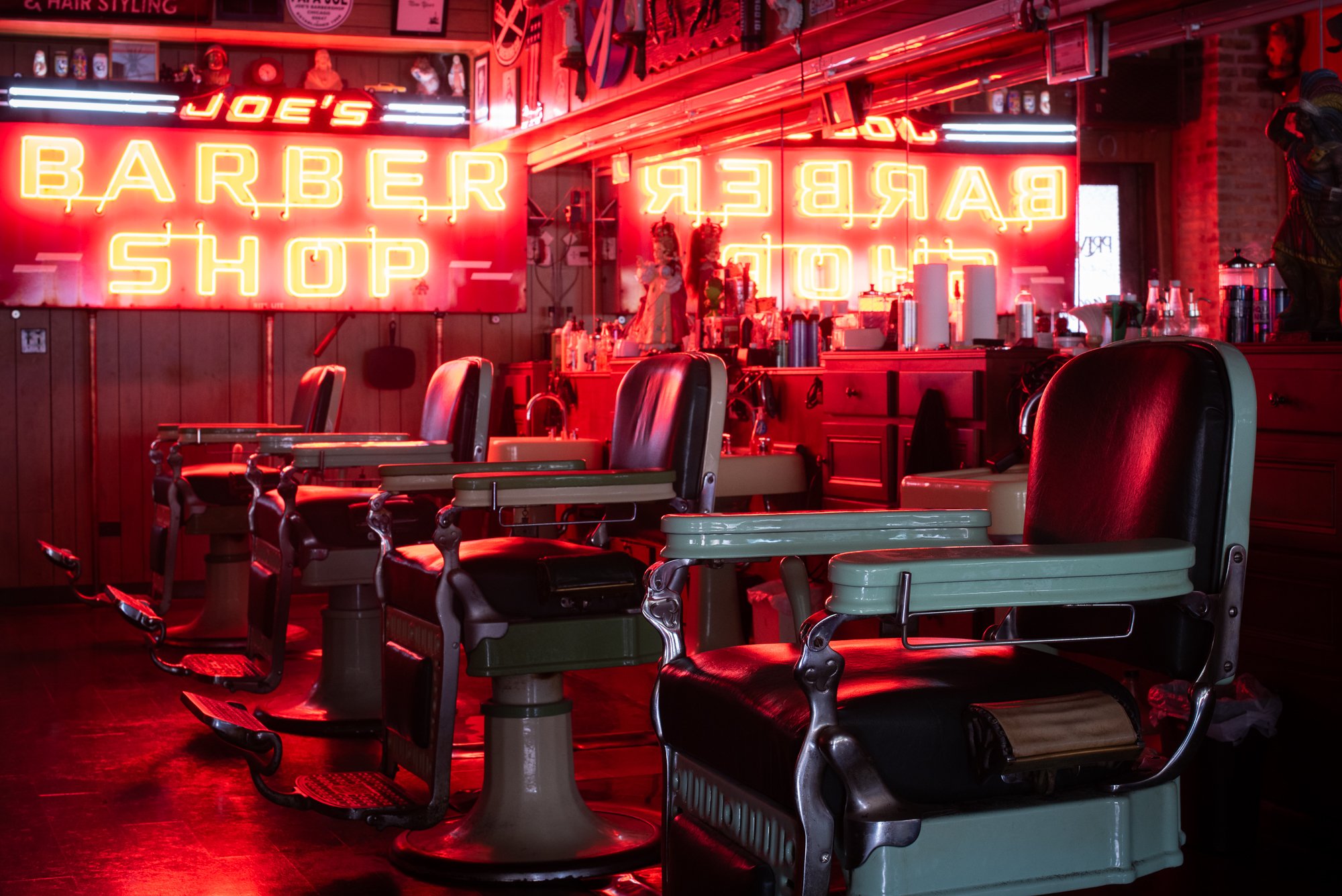 Empty barber chairs lit by the red neon sign inside Joe’s Barbershop in Chicago