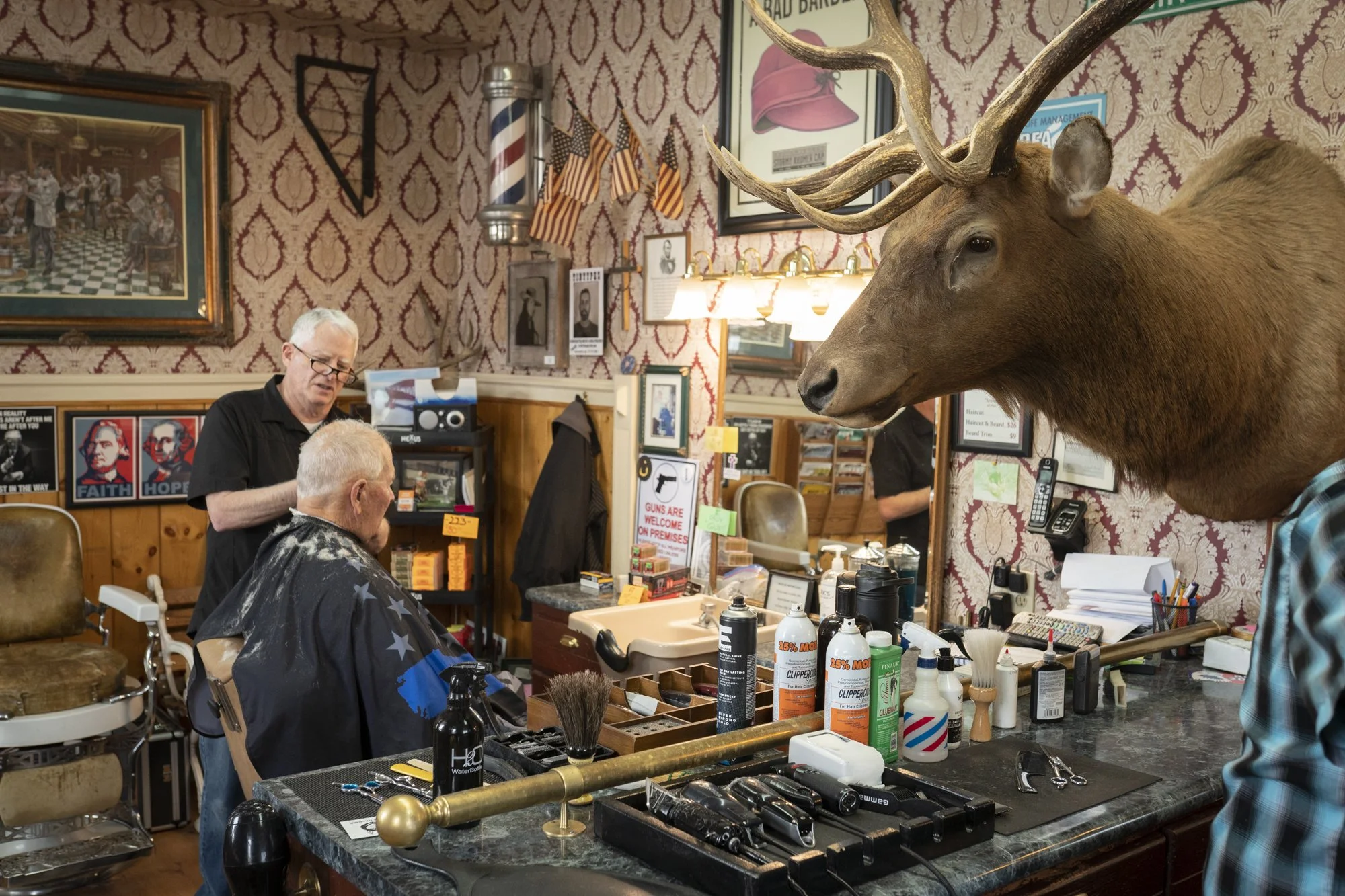 Old-school barbershop haircut beneath a mounted elk head in a traditional American barbershop interior.